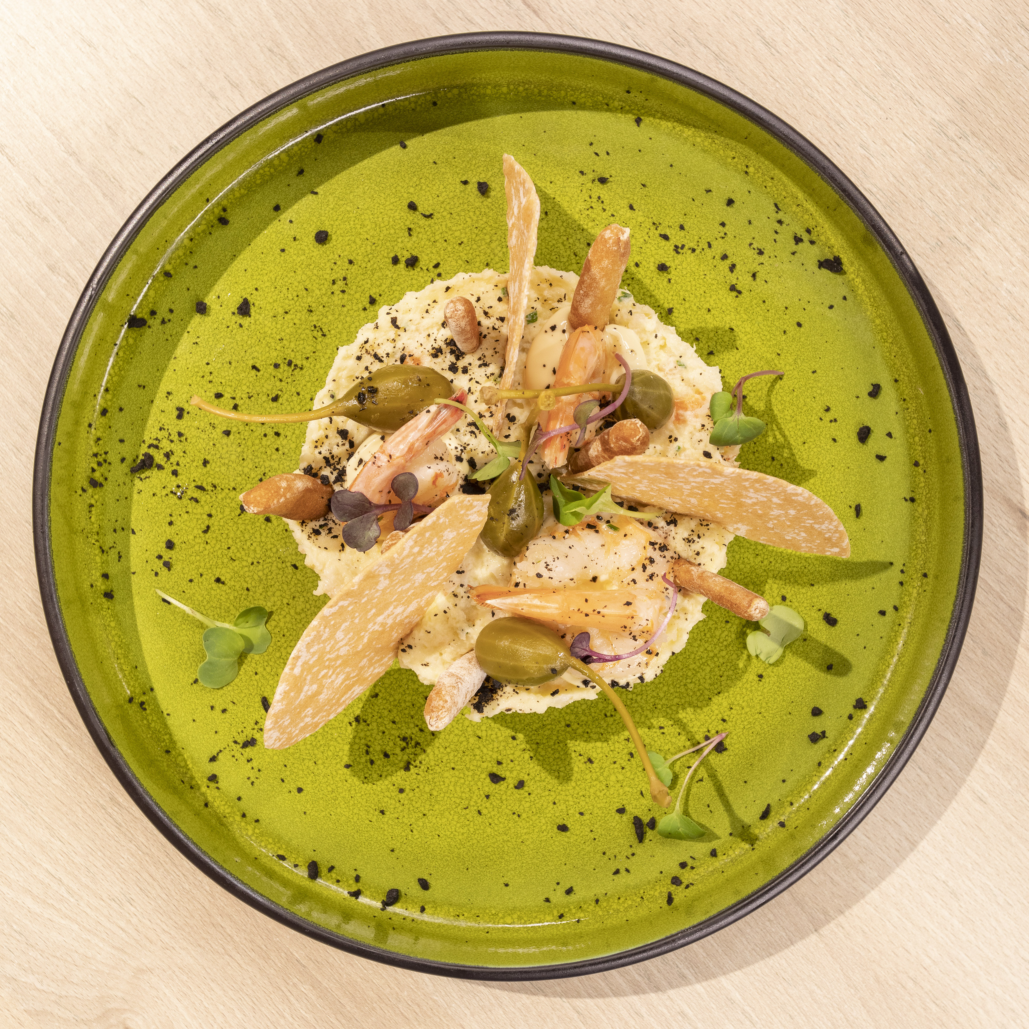 Gourmet shrimp, caper berry & crisp cracker dish on a vibrant green plate.
