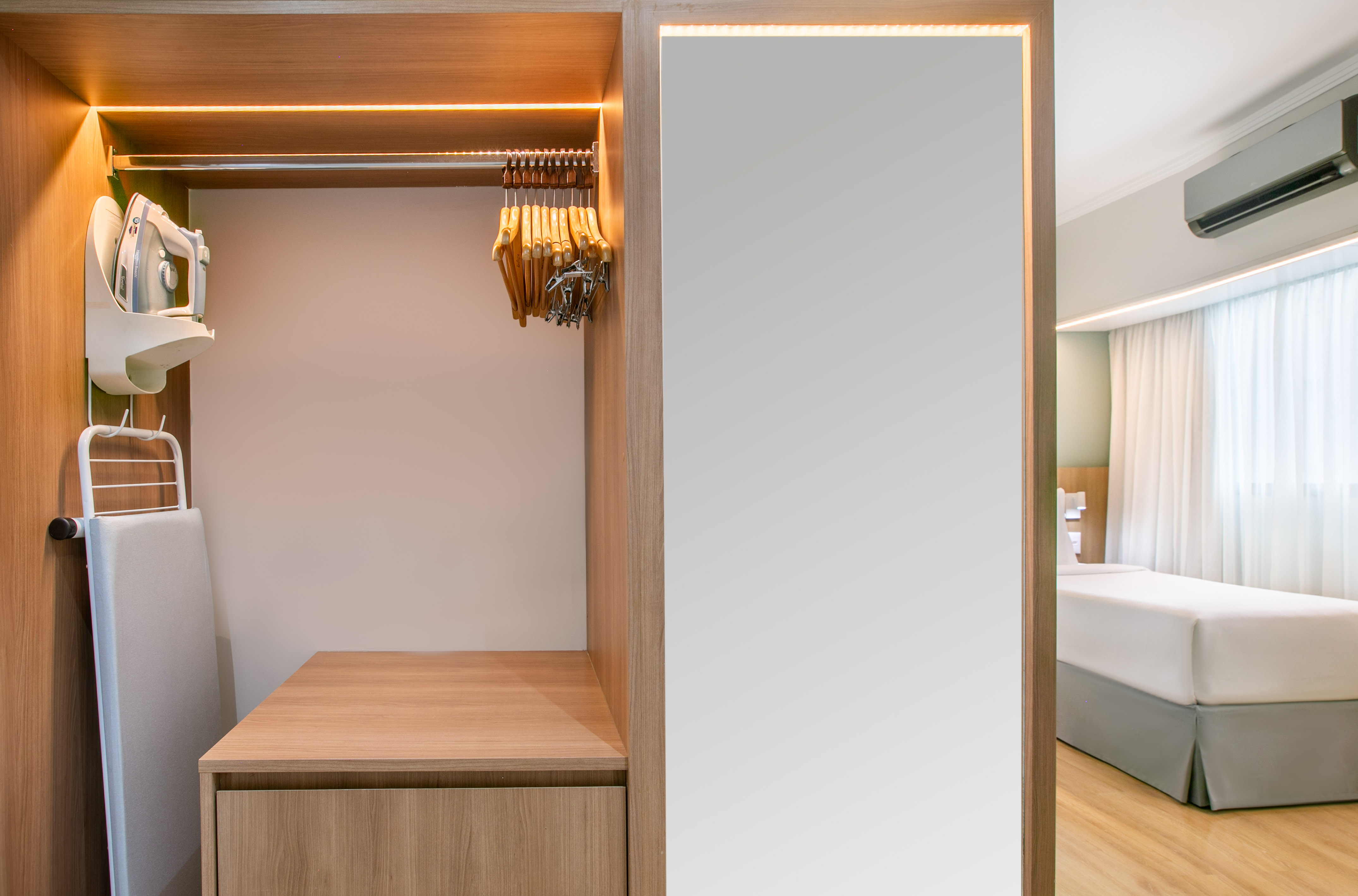 Built-in hotel closet with iron, ironing board, hangers, and full-body mirror.