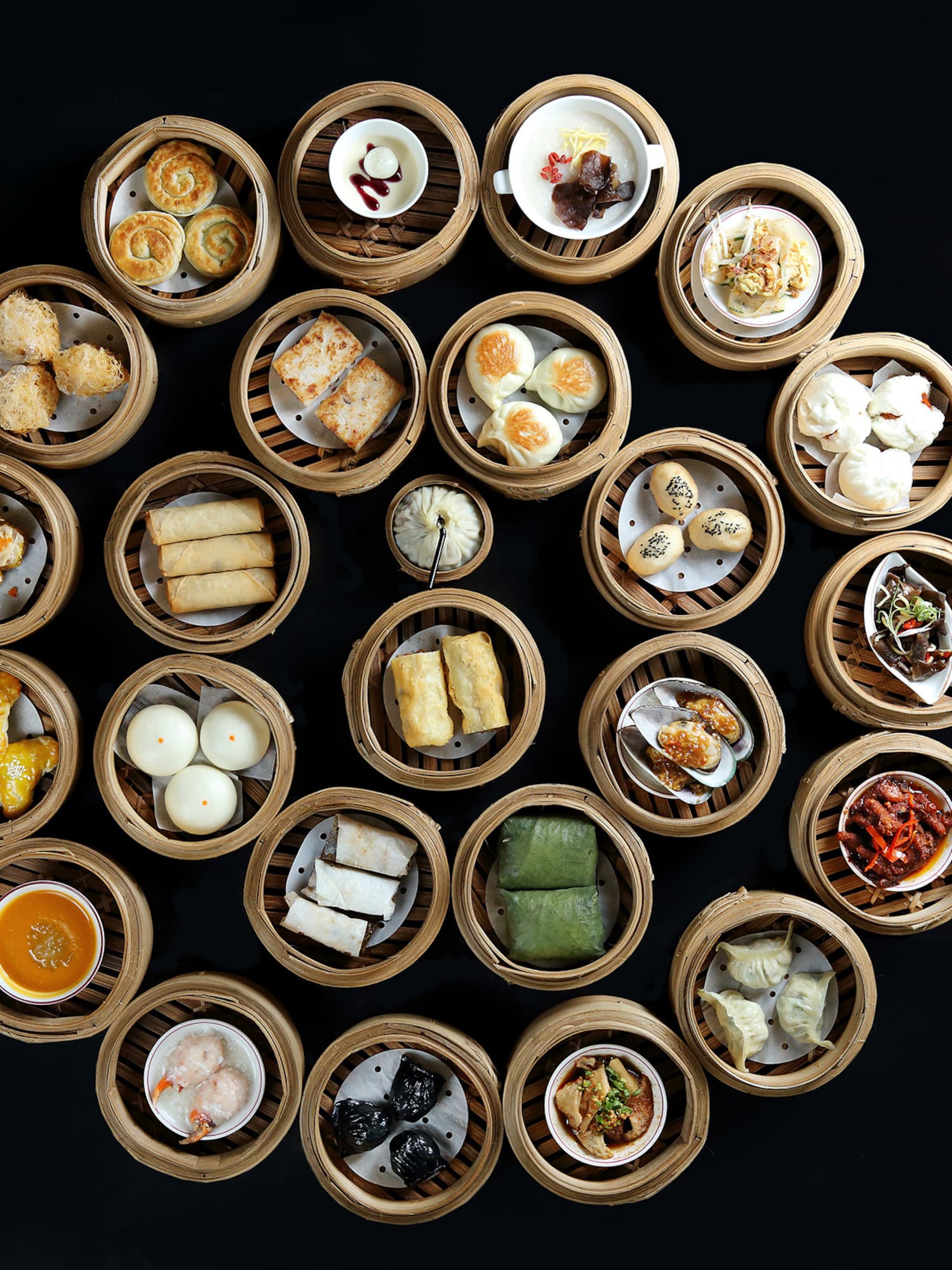 Assortment of Chinese dim sum in bamboo steamers on black background.