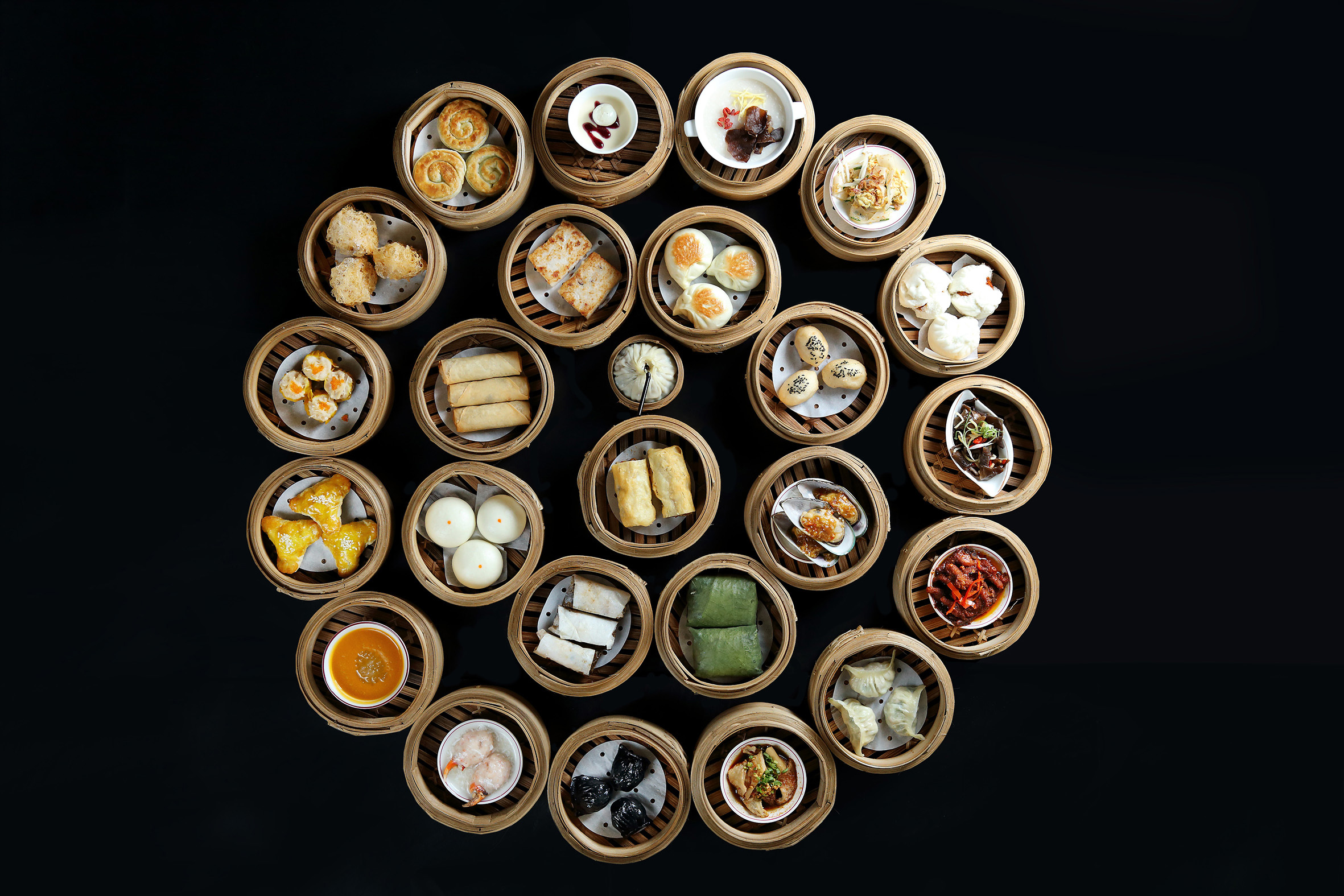 Assortment of Chinese dim sum in bamboo steamers on black background.