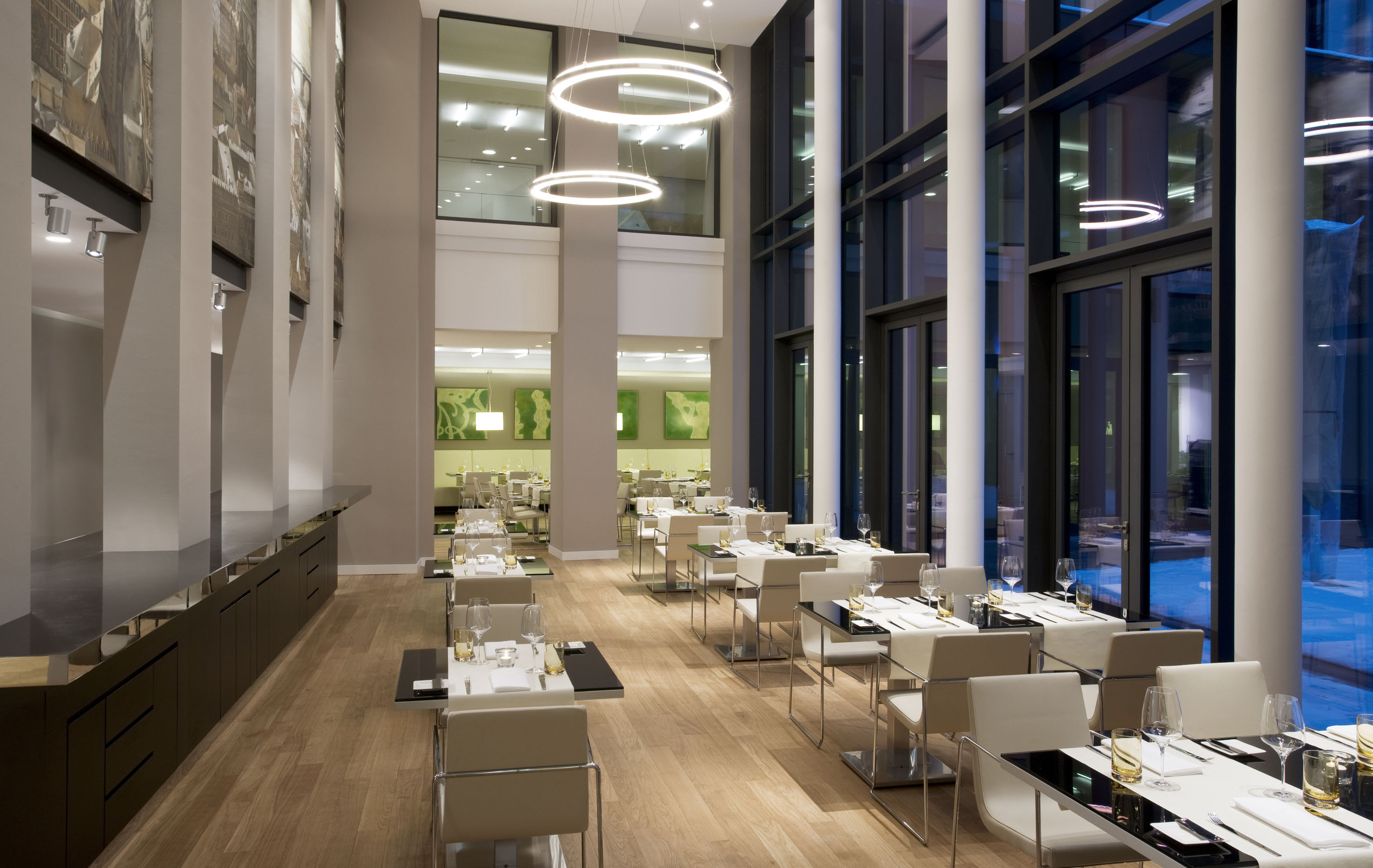 Modern restaurant with elegant table settings, wooden floor, and tall windows.
