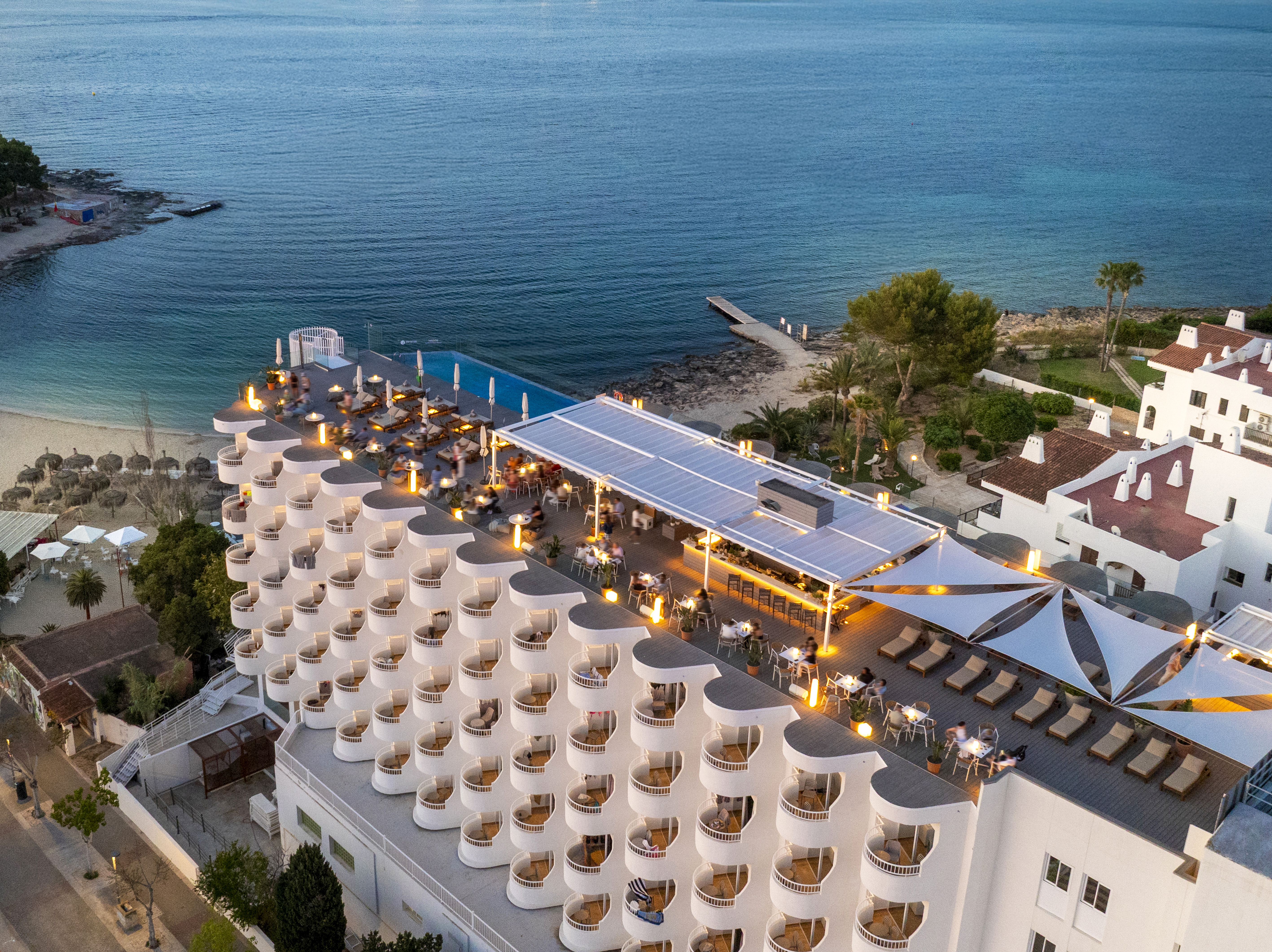 Luxury oceanfront hotel with rooftop bar, infinity pool, and lit balconies.