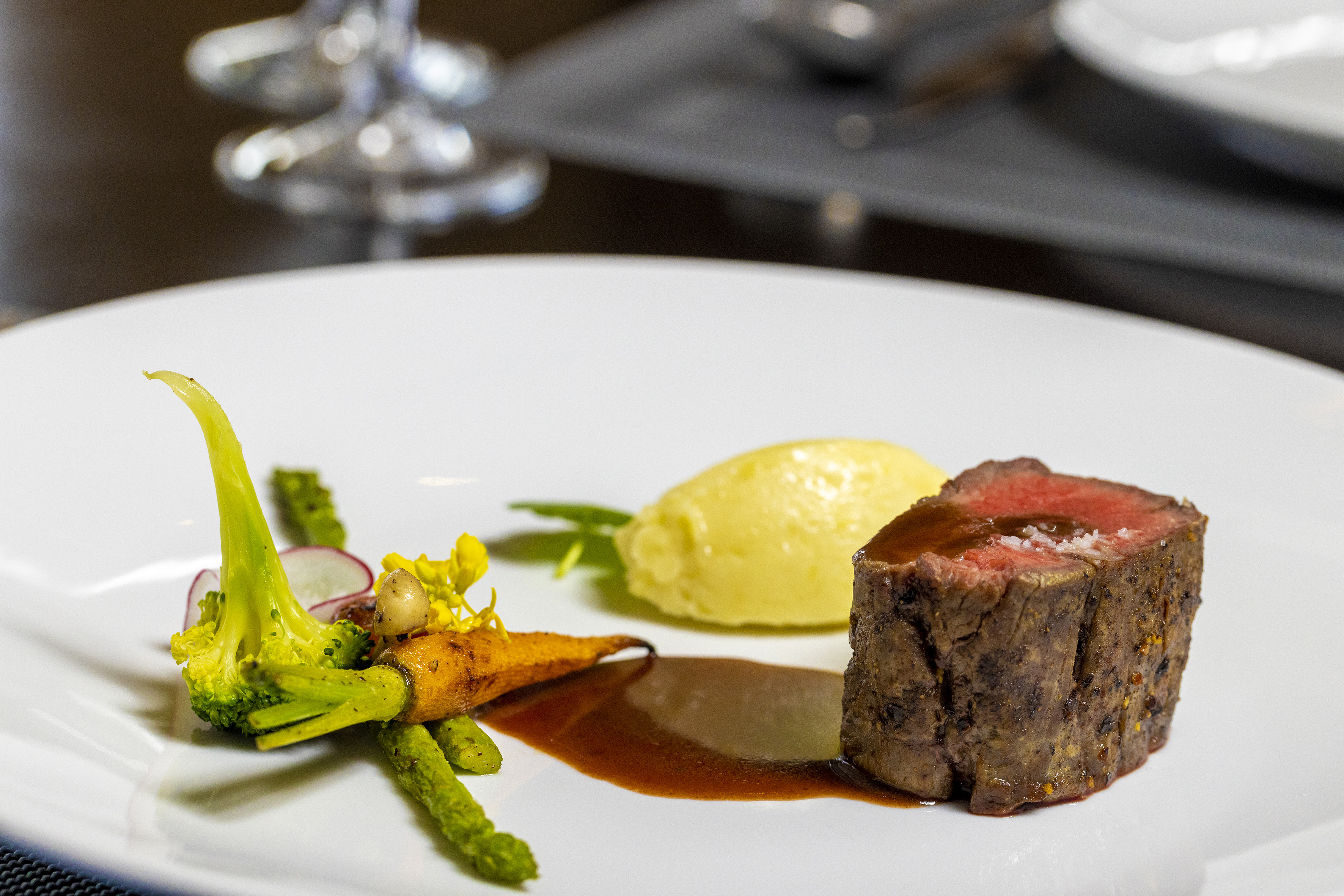 Gourmet plated steak, potato purée, broccoli, carrots, and rich jus.