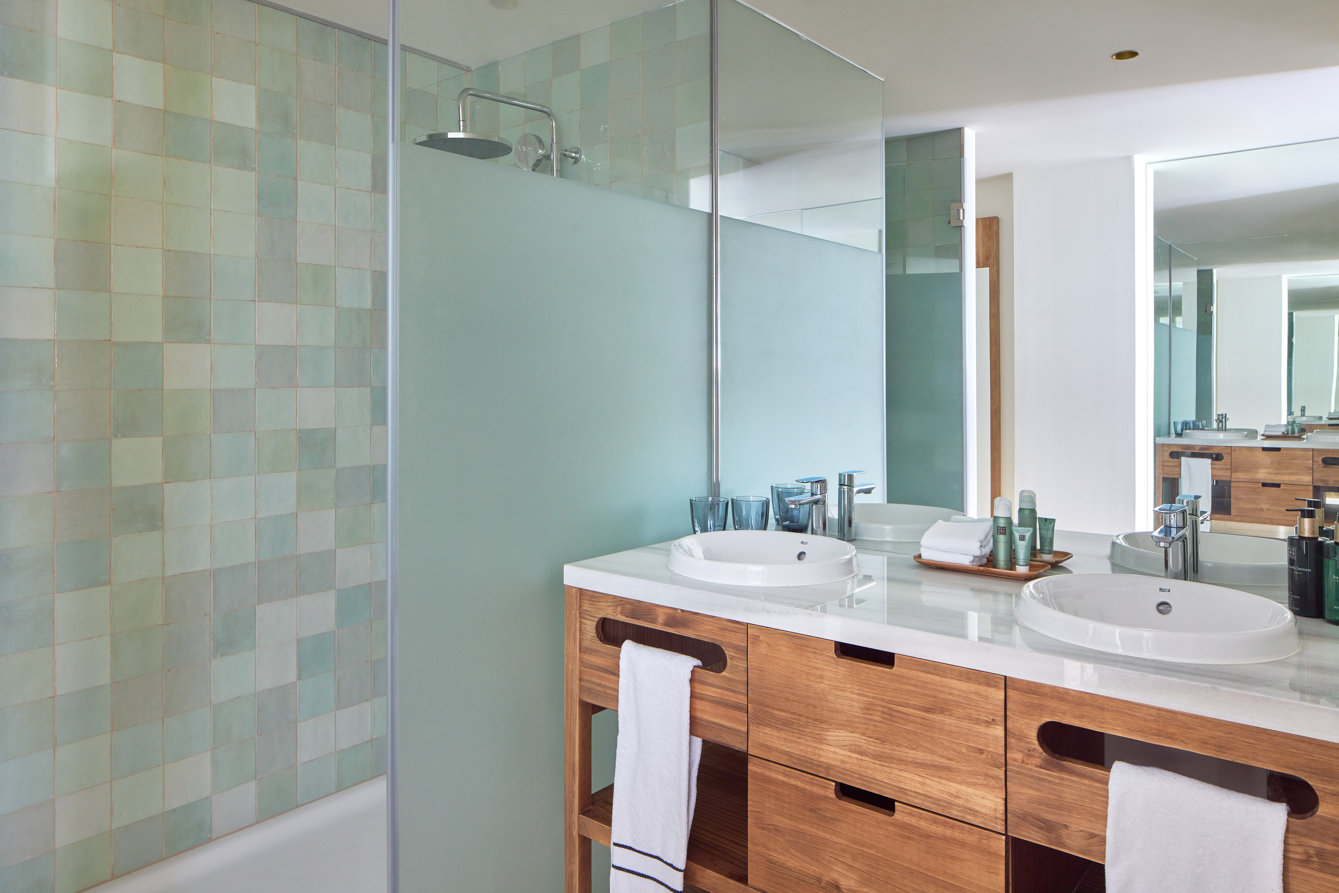 Modern double vanity bathroom with wood cabinets and green tiled shower.