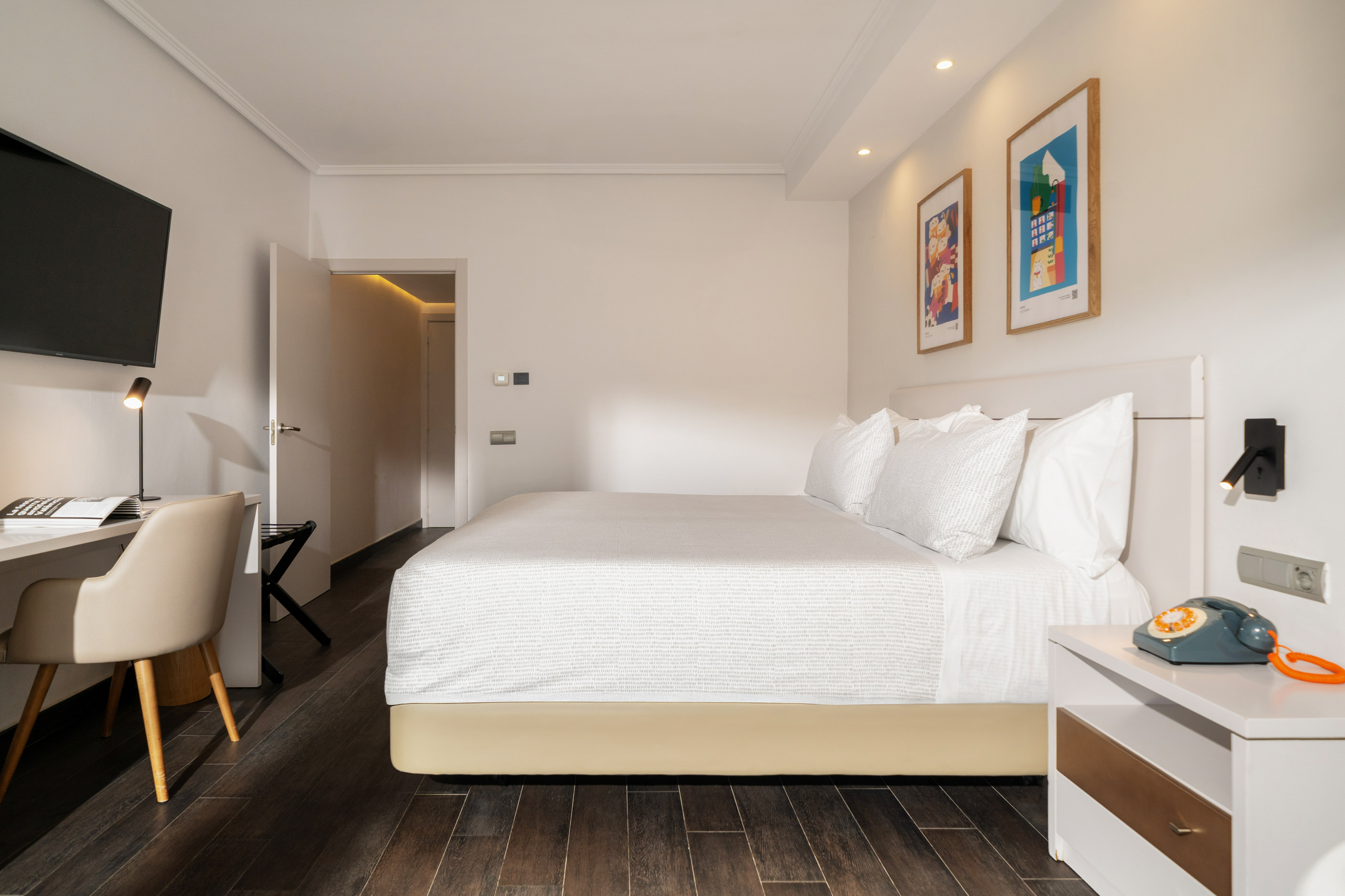 Bright hotel bedroom with king bed, desk, TV, and modern art prints.