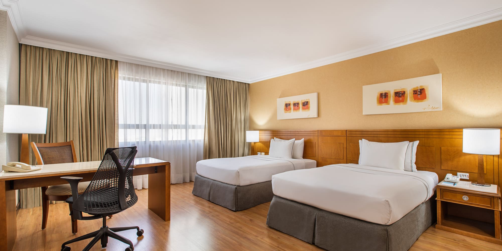 Hotel room with two twin beds, desk, office chair, and wooden floors.