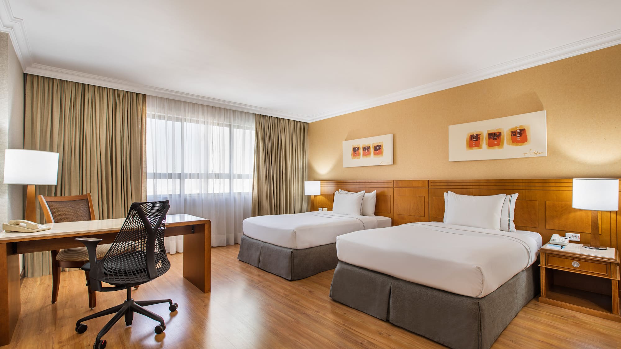 Comfortable hotel room with two twin beds, wooden desk, and modern office chair.