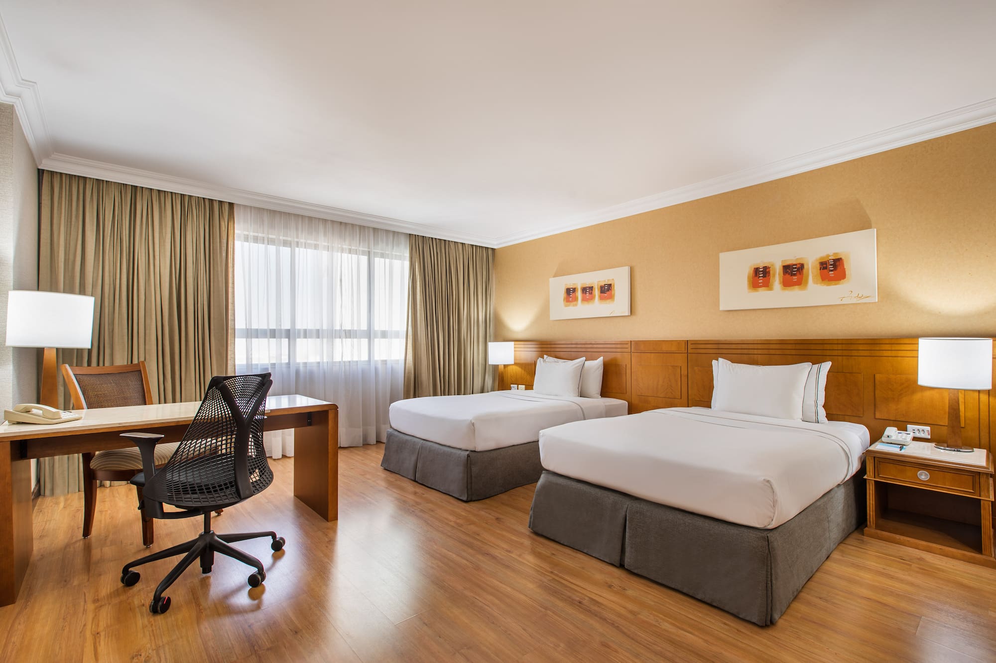 Comfortable hotel room with two twin beds, wooden desk, and modern office chair.