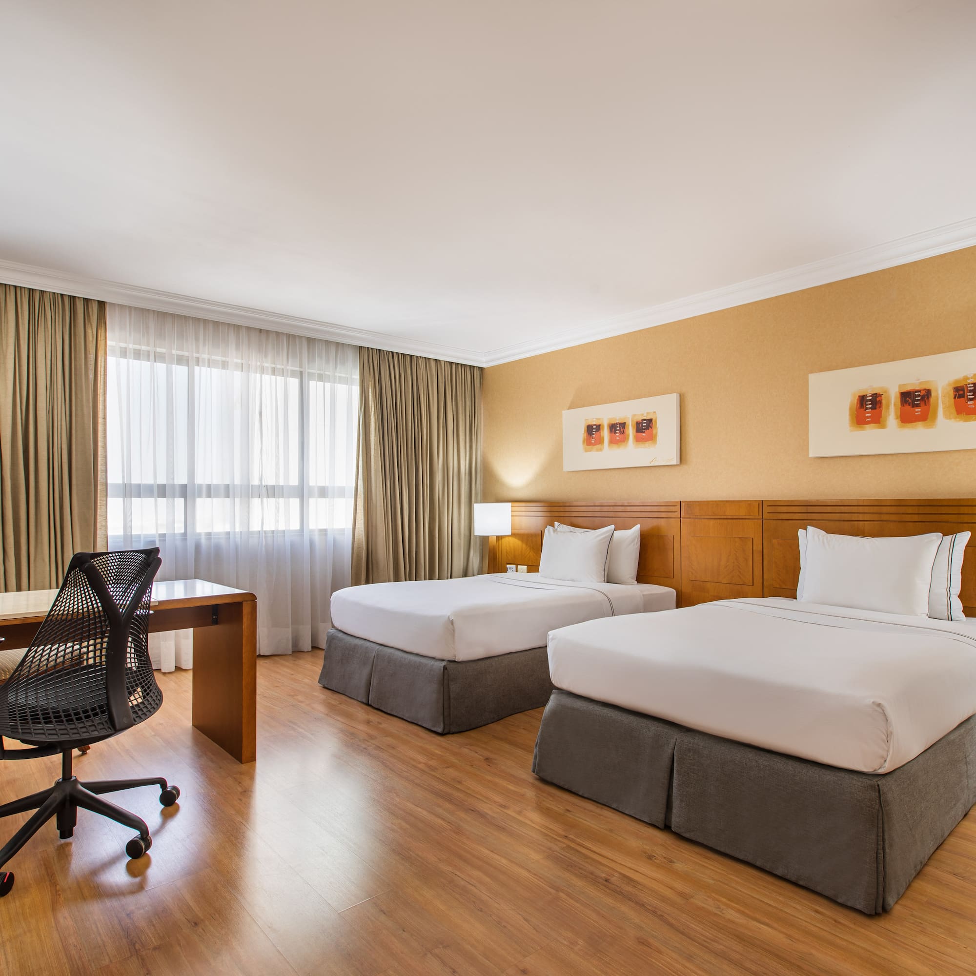 Comfortable hotel room with two twin beds, wooden desk, and modern office chair.