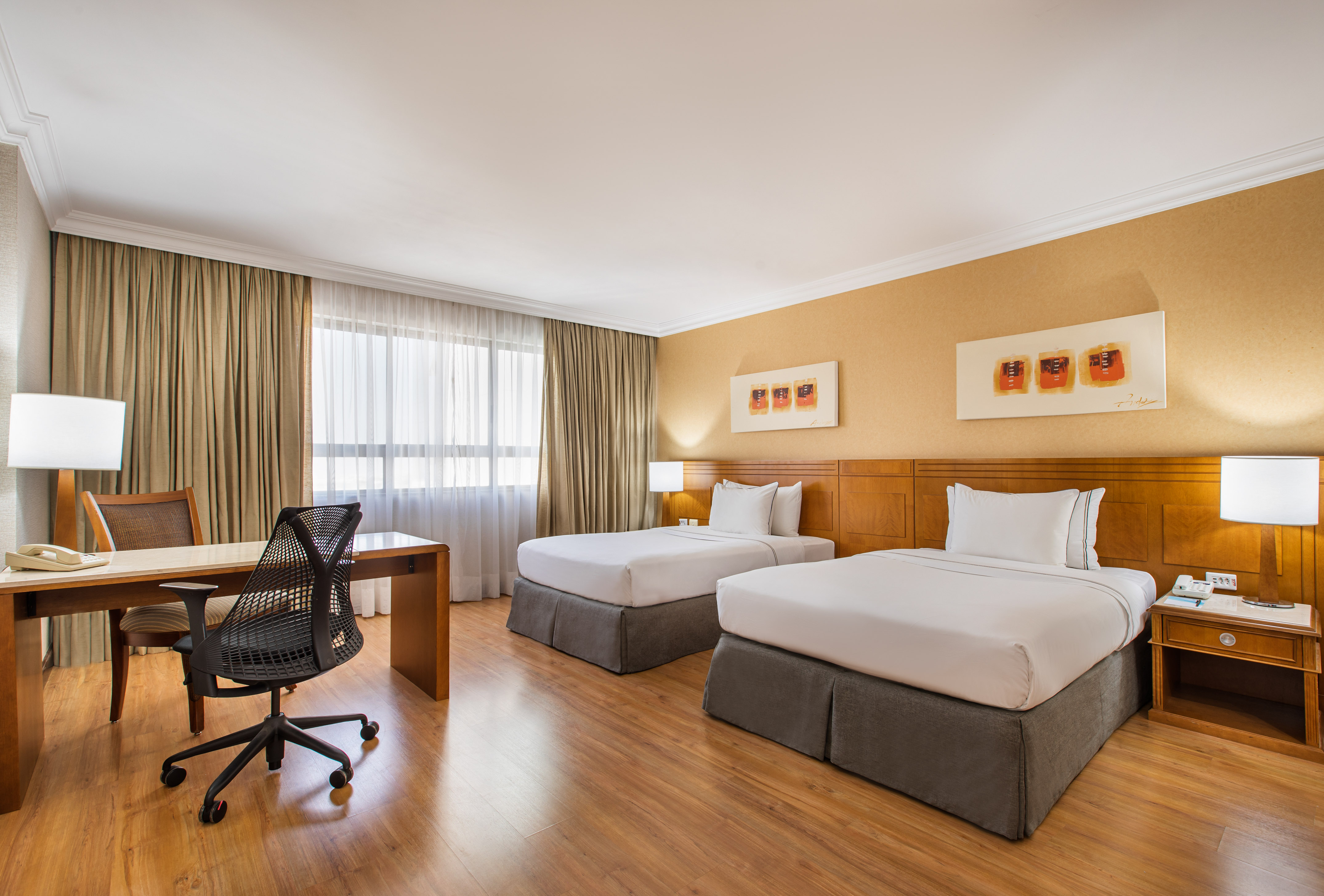 Comfortable hotel room with two twin beds, wooden desk, and modern office chair.