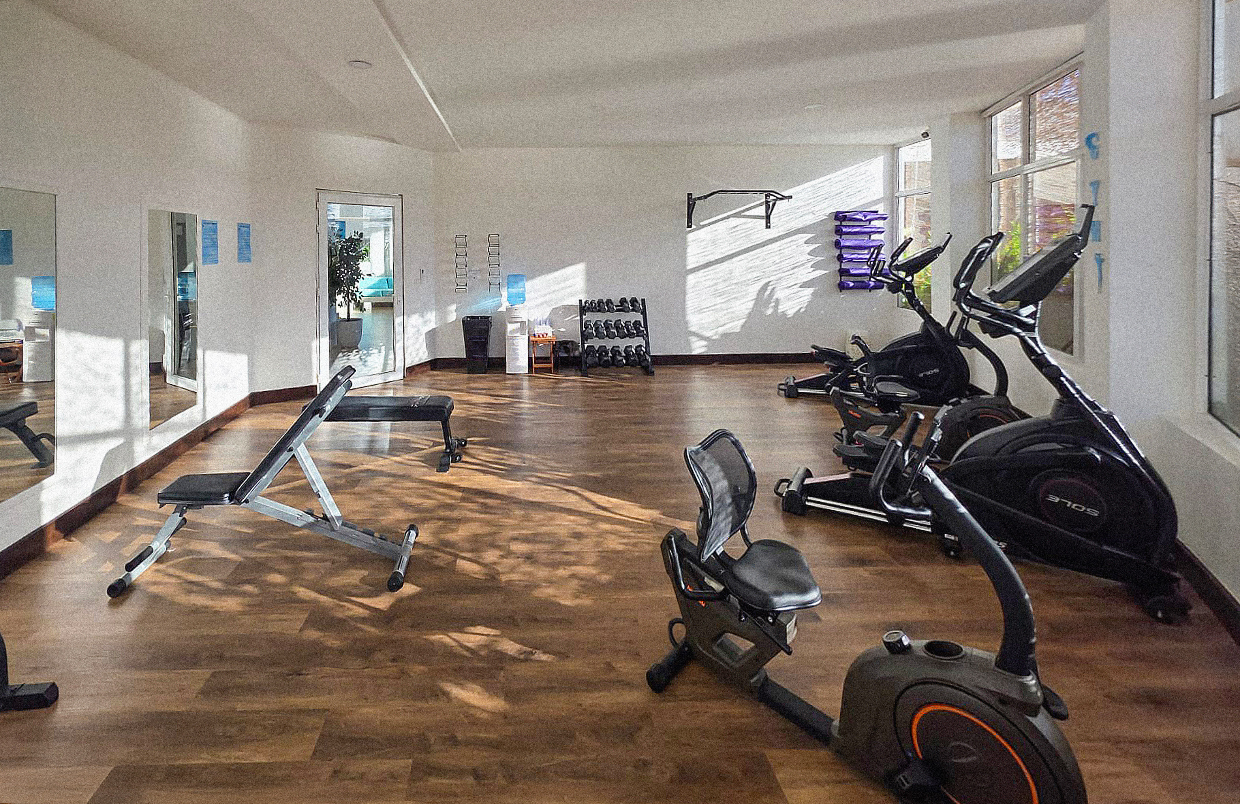 Well-lit hotel gym with ellipticals, recumbent bike, weights, and workout bench.