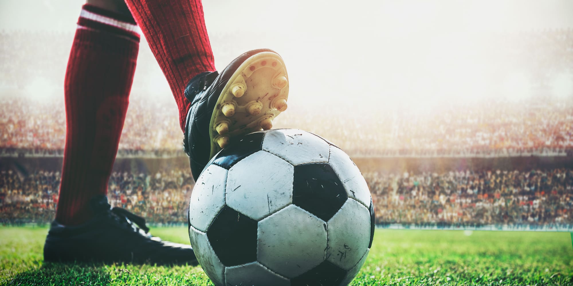 Player's cleated foot on soccer ball on grass field with stadium lights.