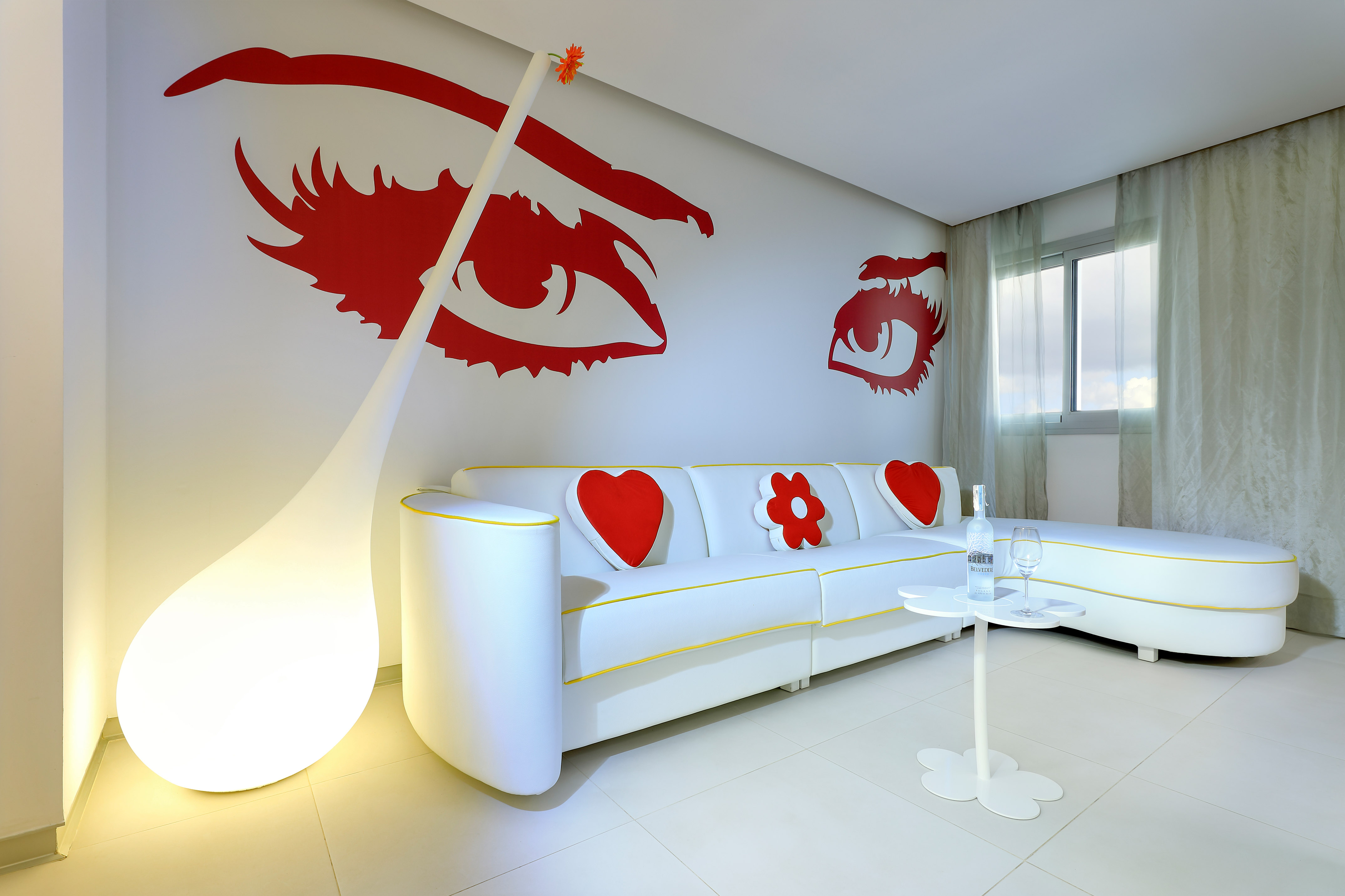Modern living room with white sofa, bold red eye wall art, and teardrop floor lamp.