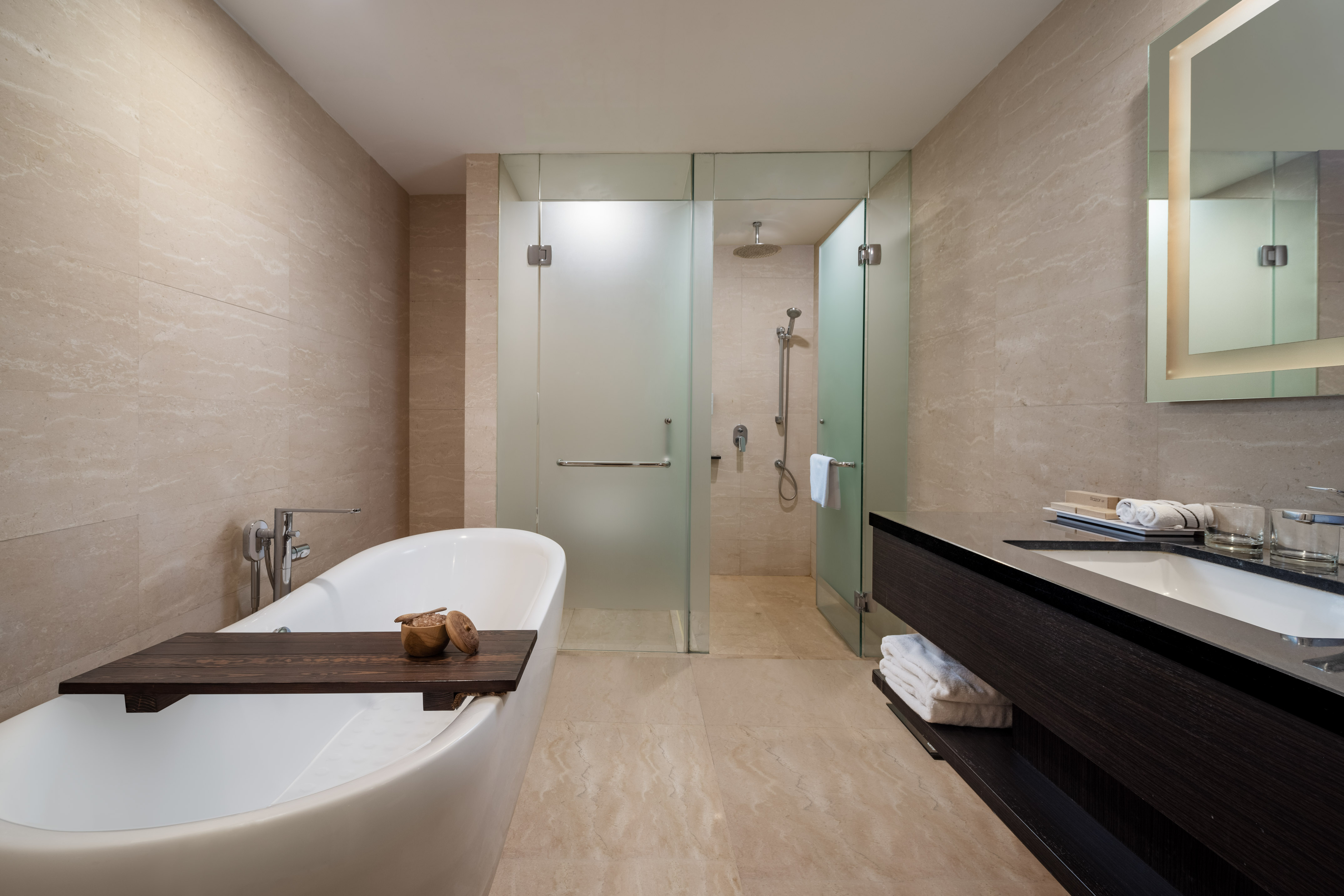 Modern bathroom with freestanding tub, glass shower, dark wood vanity, and stone tiles.