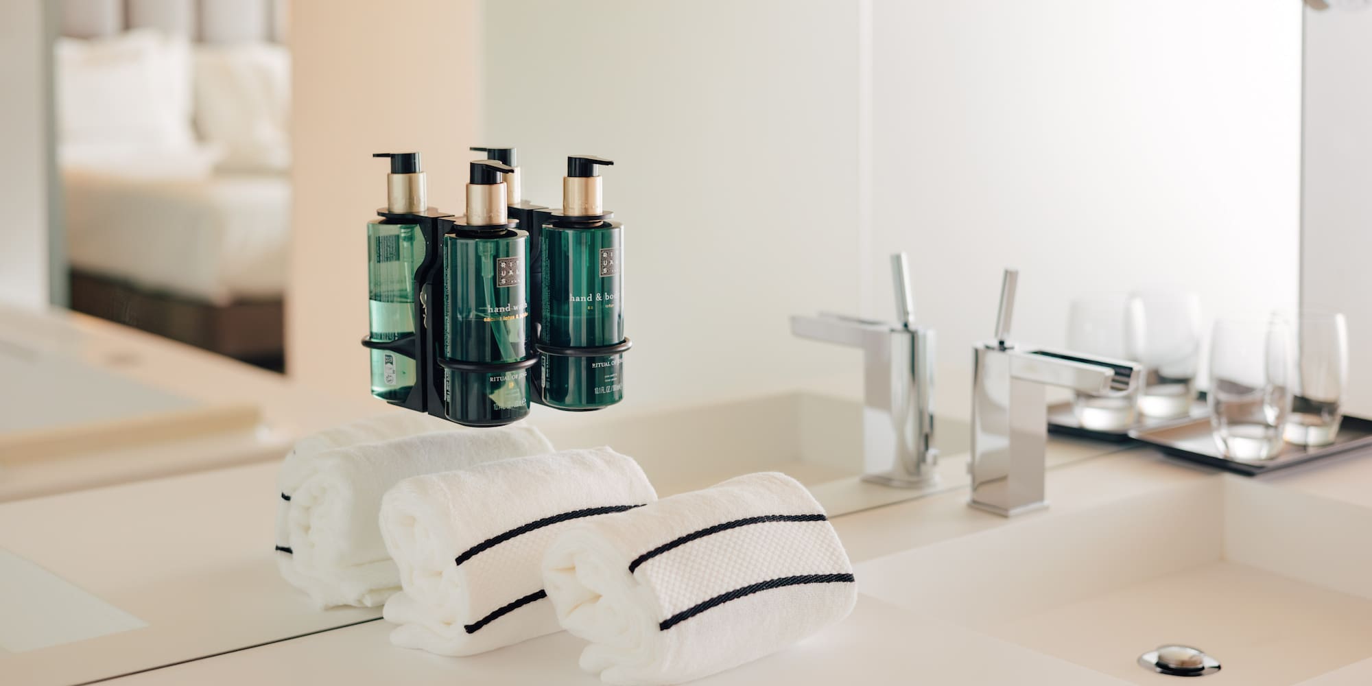 Hotel bathroom vanity: green pump soaps, white striped towels, chrome faucets.