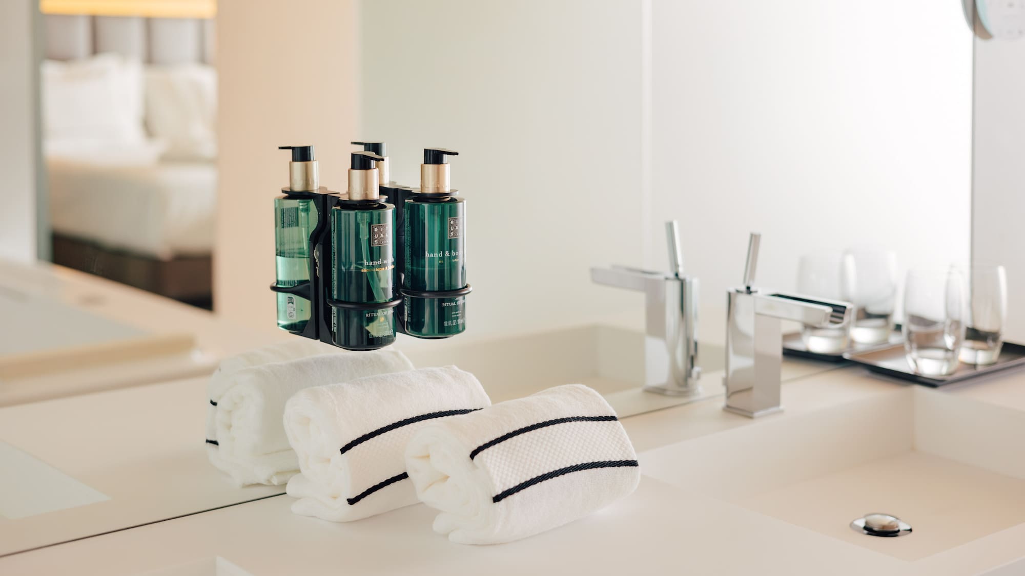 Hotel bathroom vanity: green pump soaps, white striped towels, chrome faucets.