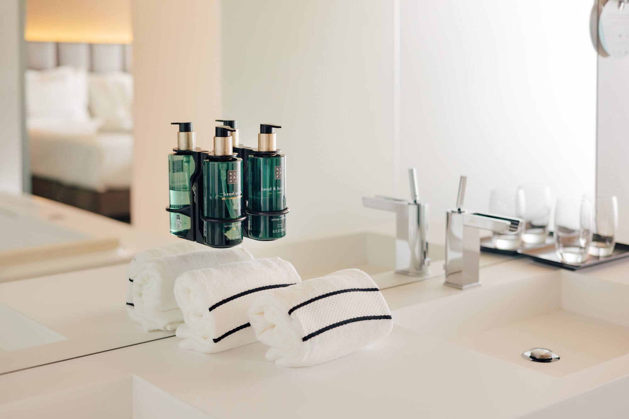 Hotel bathroom vanity: green pump soaps, white striped towels, chrome faucets.