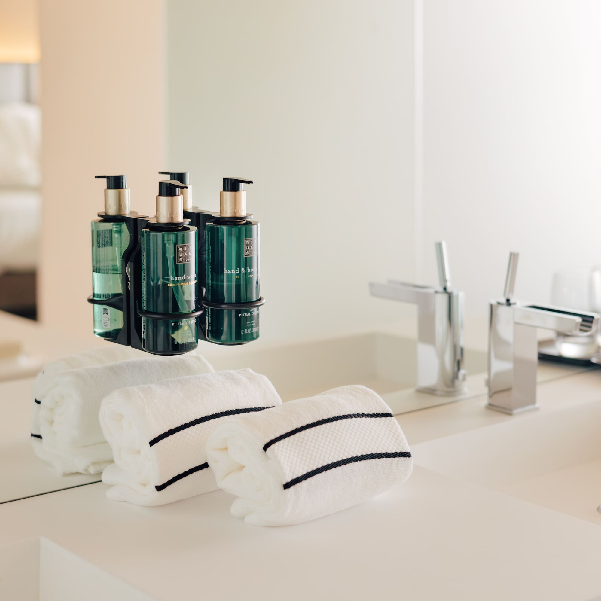 Hotel bathroom vanity: green pump soaps, white striped towels, chrome faucets.