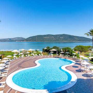 a pool with chairs and umbrellas by a body of water