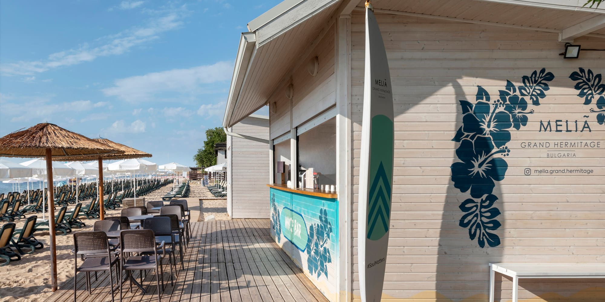 a small beach bar with chairs and a surfboard