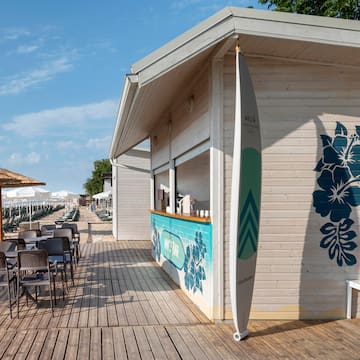 a small beach bar with chairs and a surfboard
