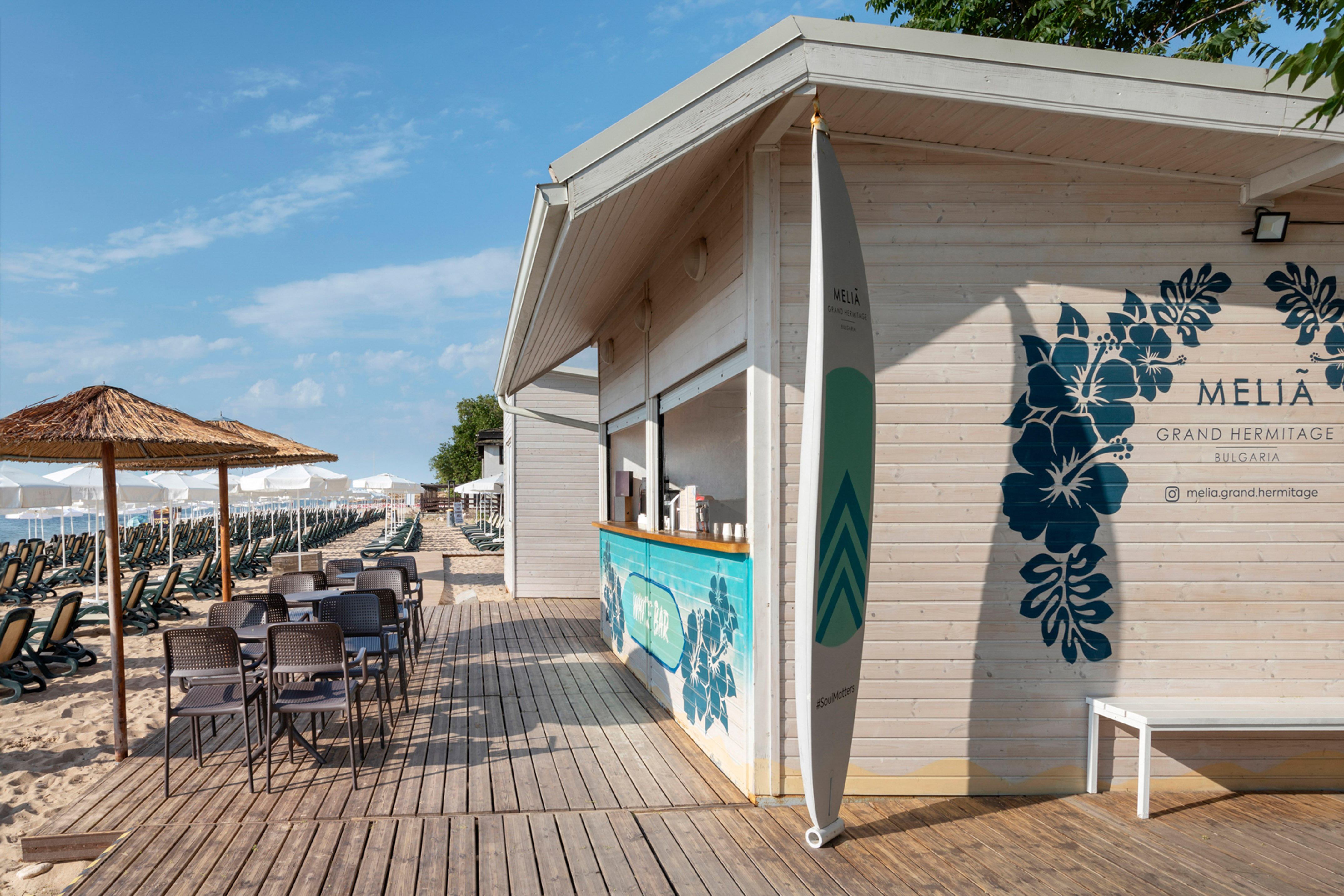 a small beach bar with chairs and a surfboard
