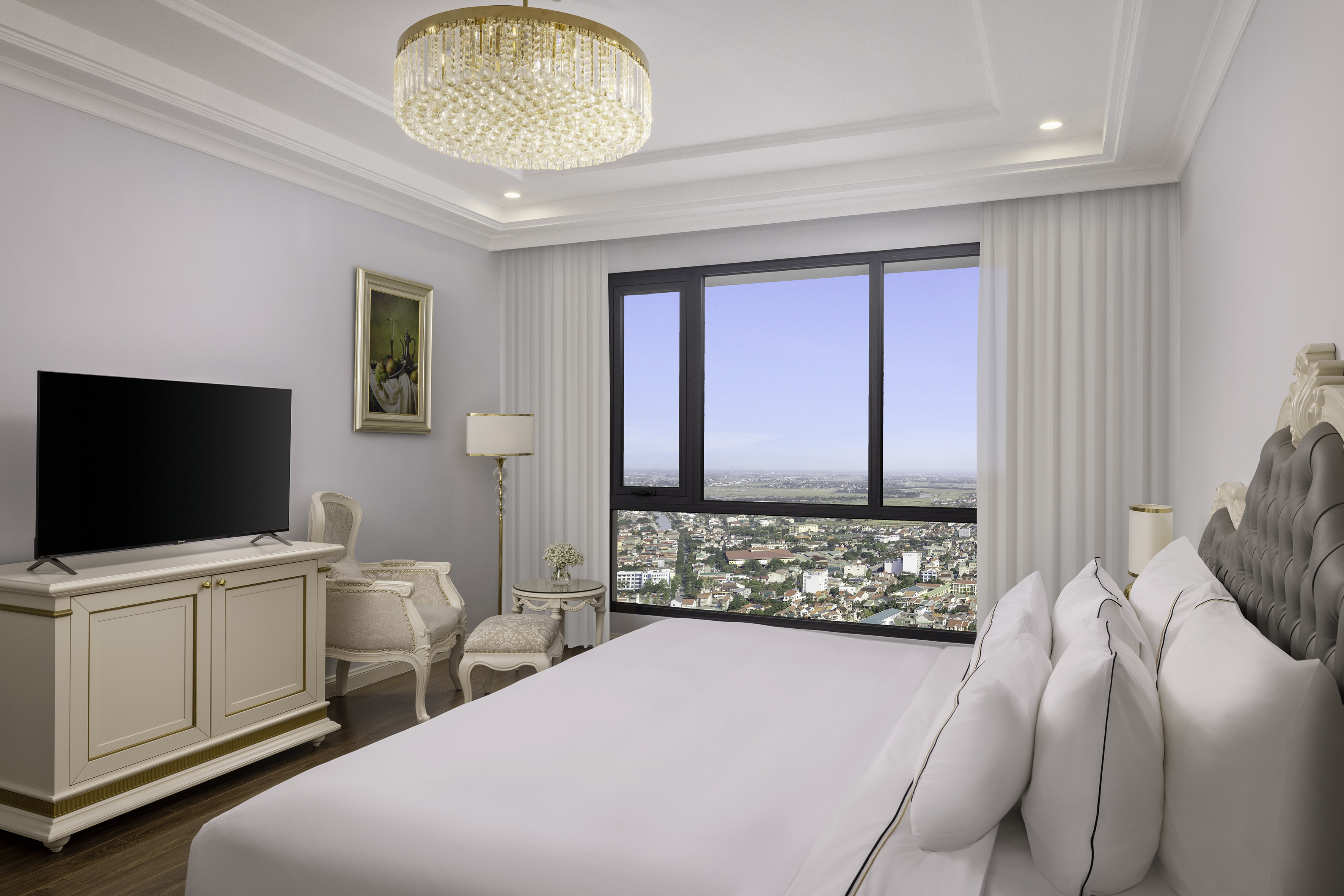 Luxurious bedroom with cityscape view, bed, TV, and elegant chandelier.