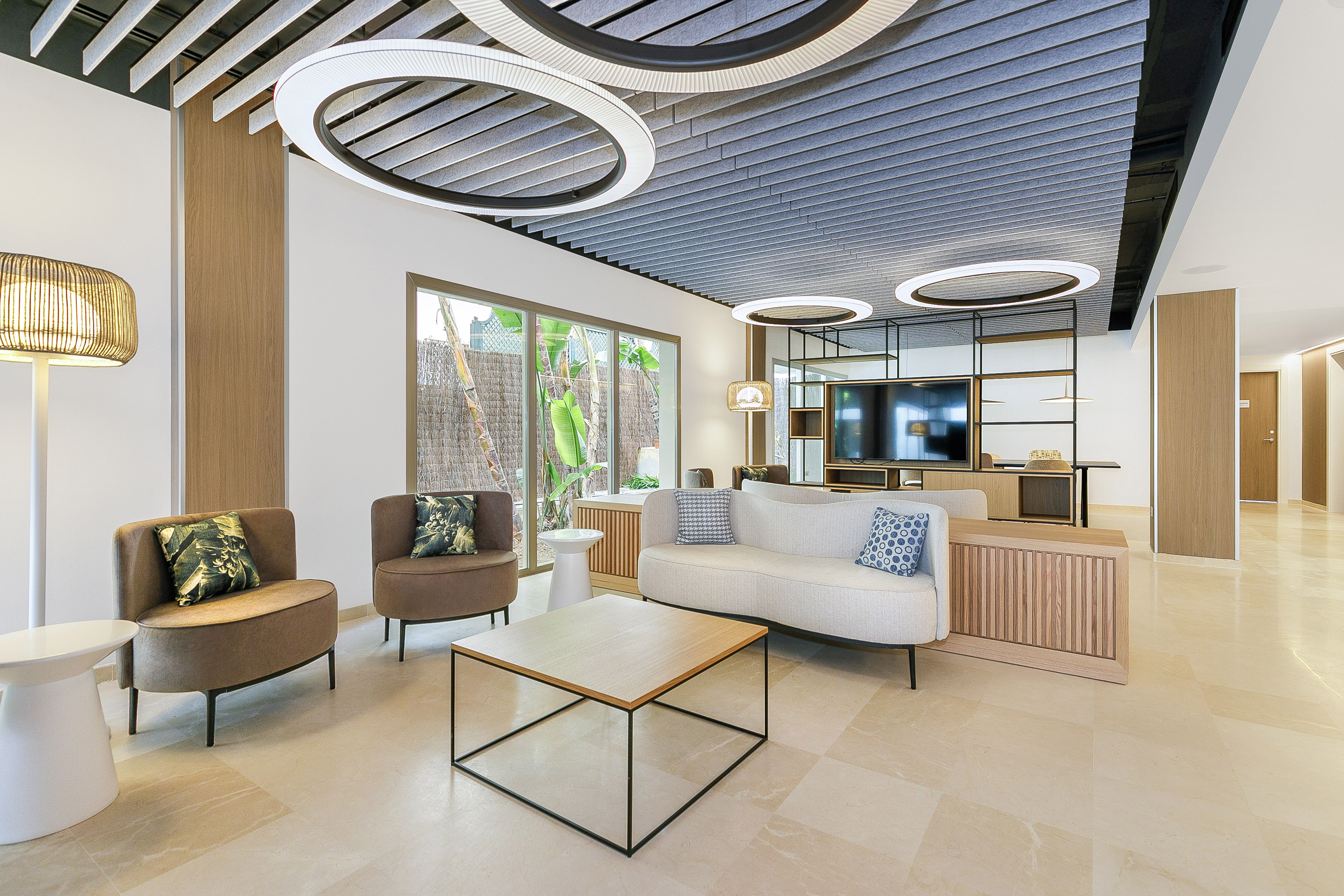 Stylish hotel lobby with modern seating, acoustic ceiling, and garden view.