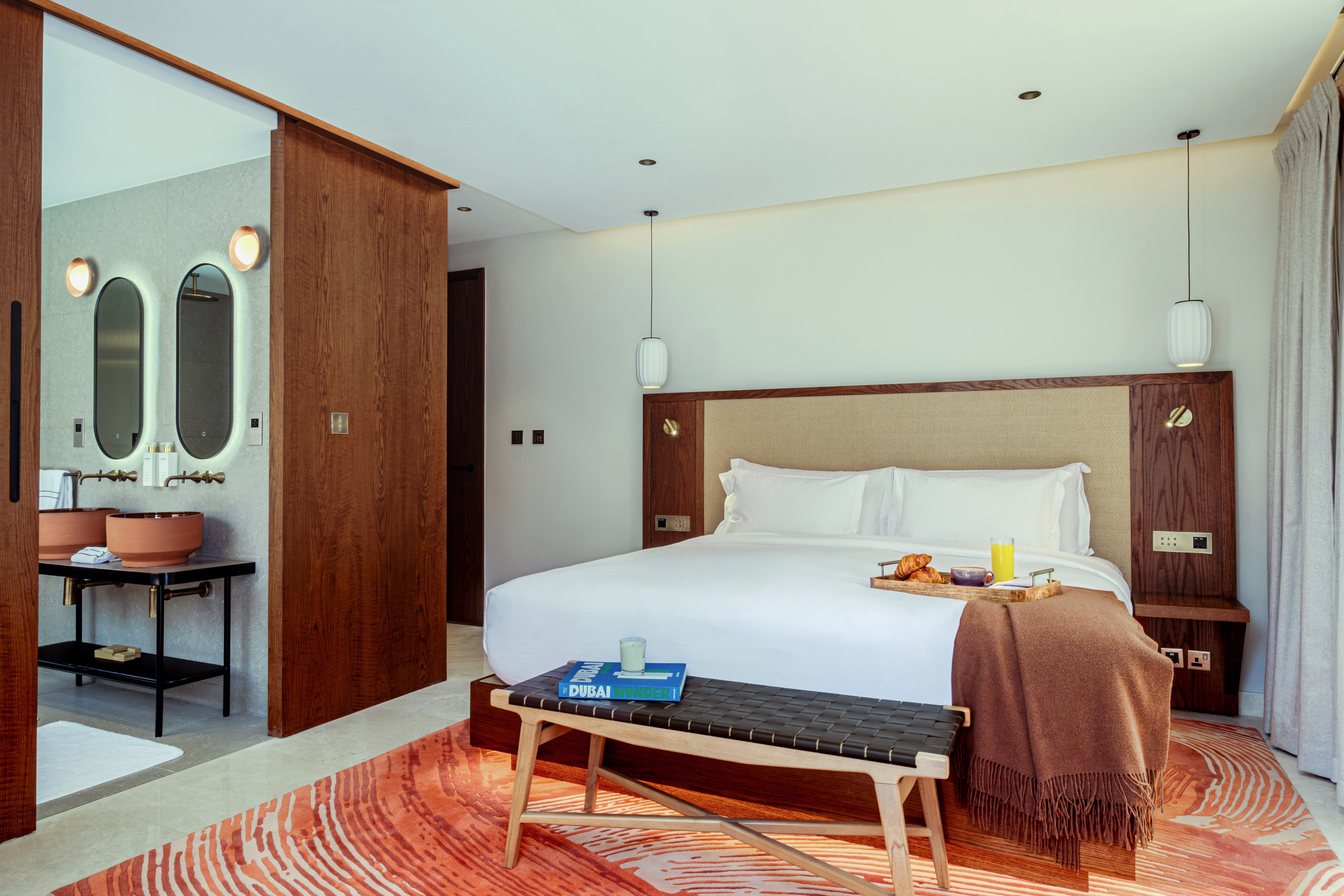 Contemporary bedroom with breakfast in bed, orange rug, and open vanity.