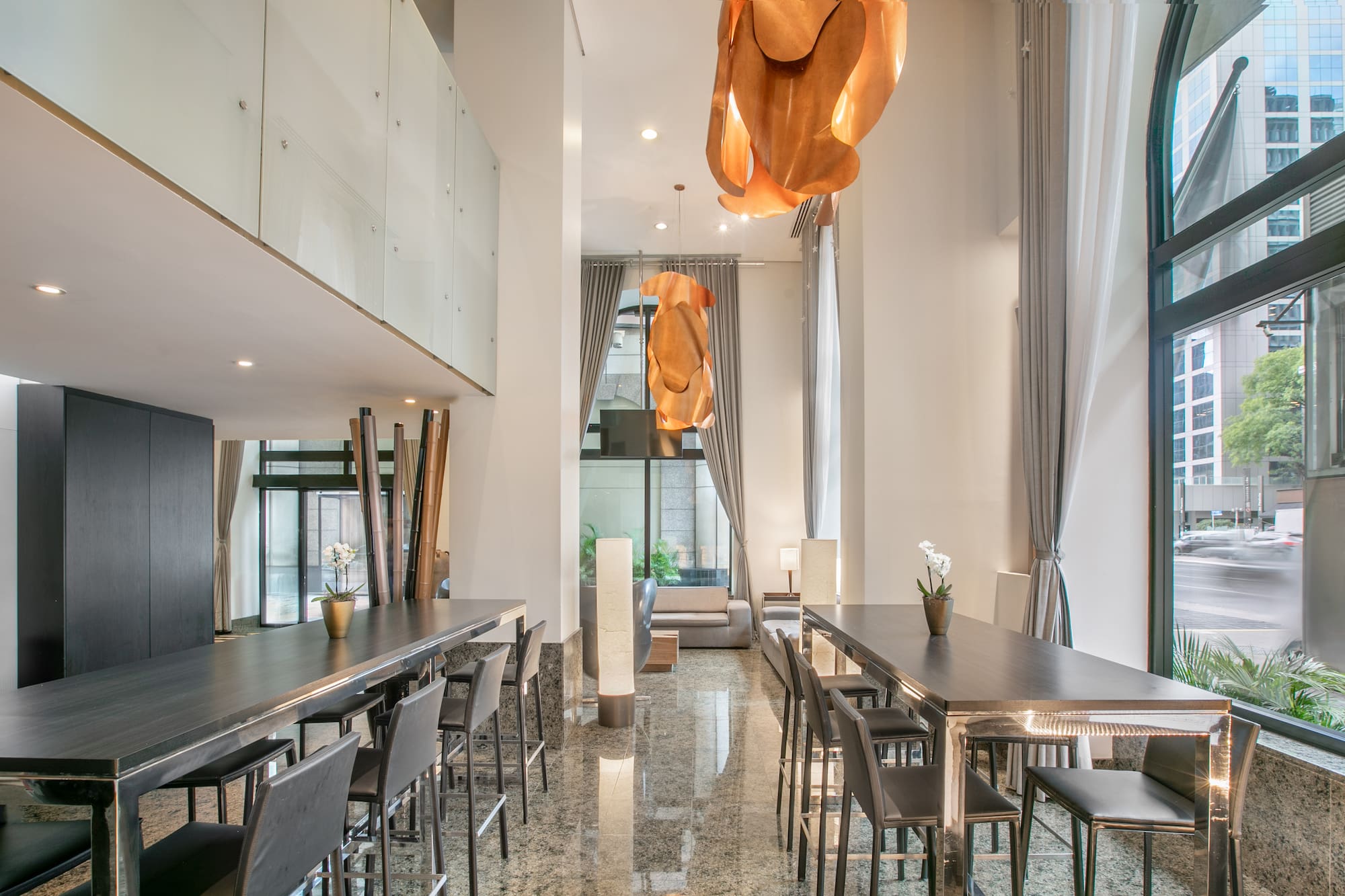 Contemporary lounge with communal bar tables, stools, and city views.