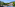 Colorful pedal boats on a lake with a waterside restaurant and green trees.