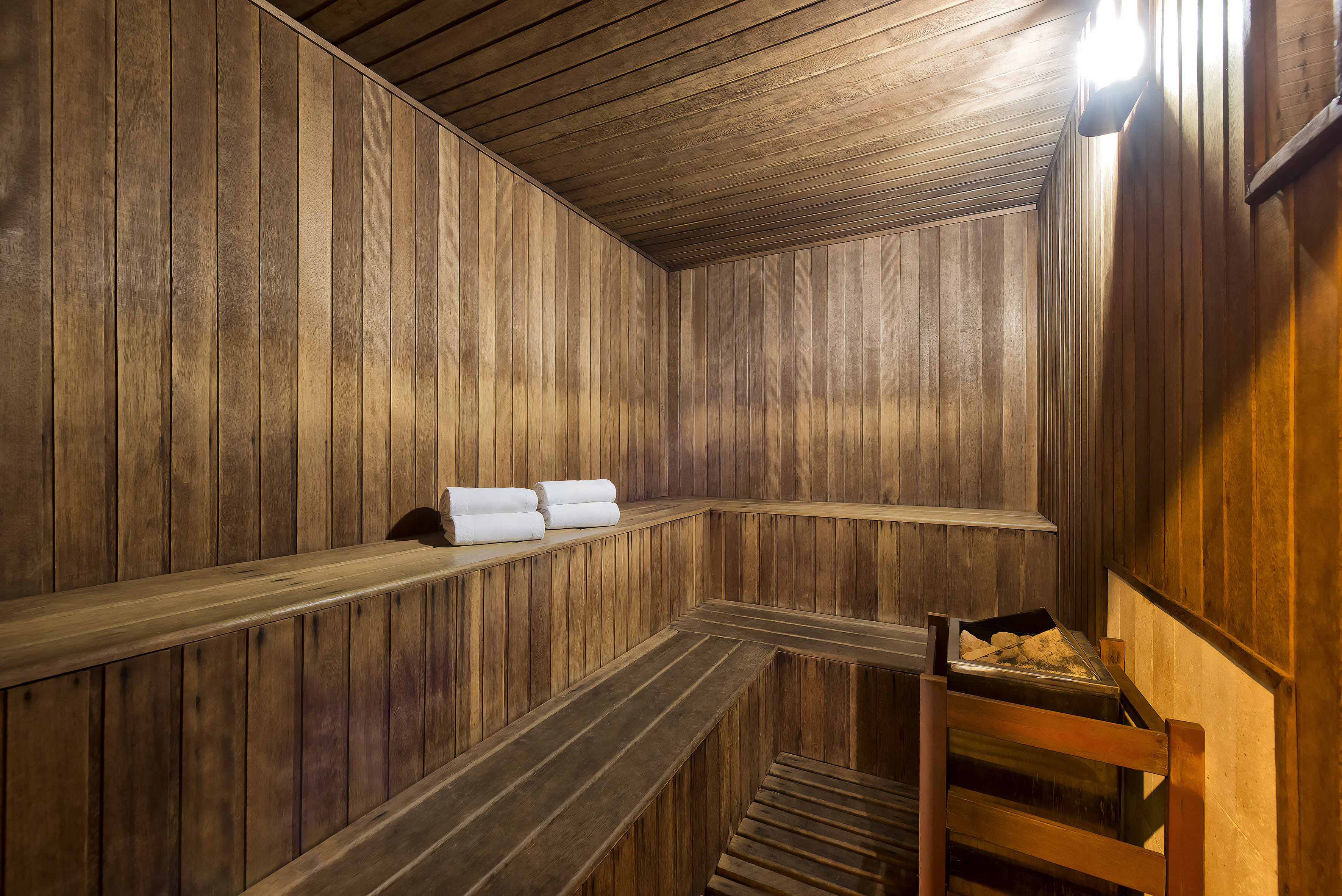 Wooden sauna with multiple benches, white rolled towels, and a rock heater.