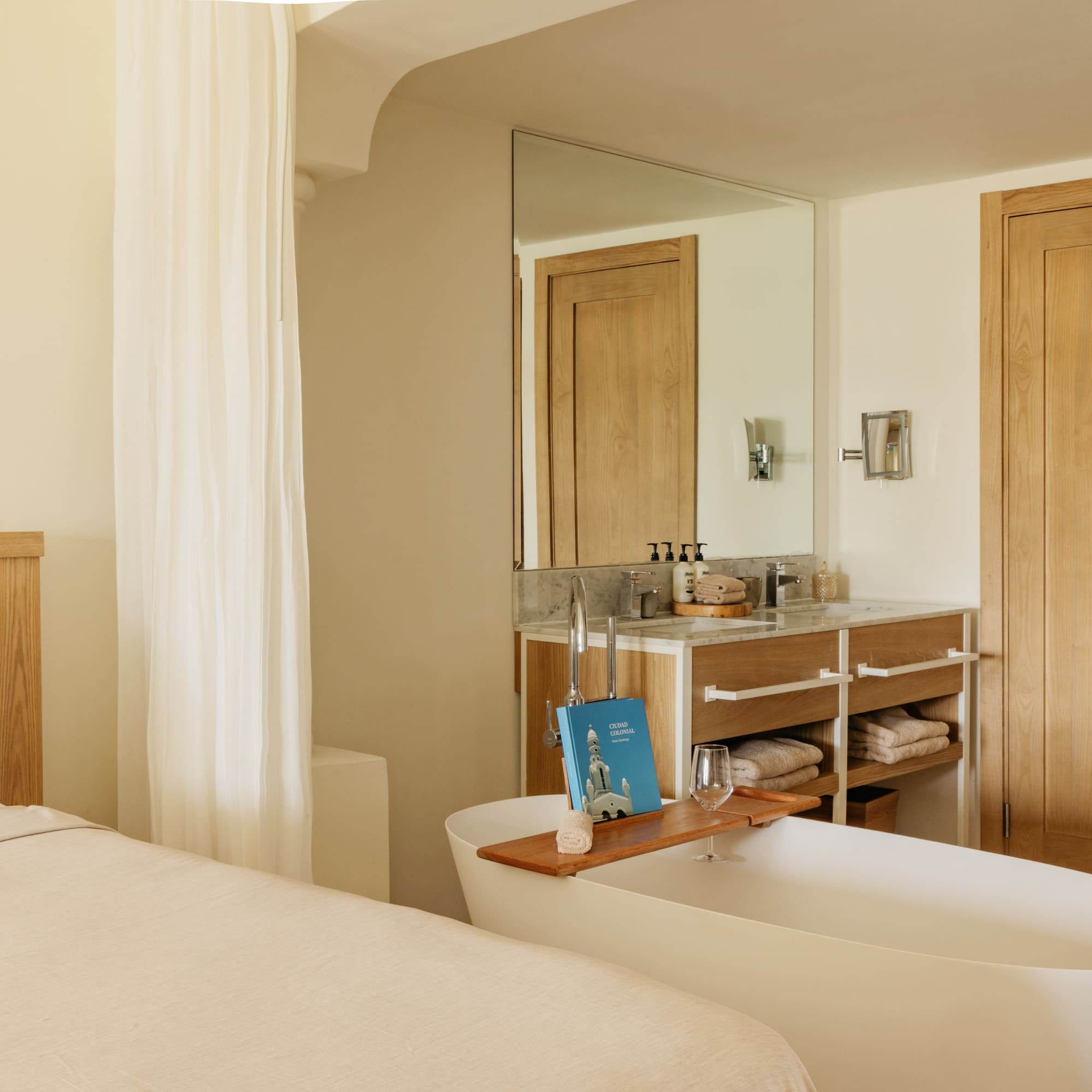 Spa-like hotel suite with bed, freestanding tub, and wooden vanity.