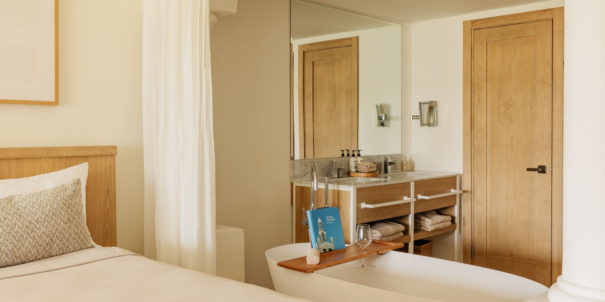 Spa-like hotel suite with bed, freestanding tub, and wooden vanity.