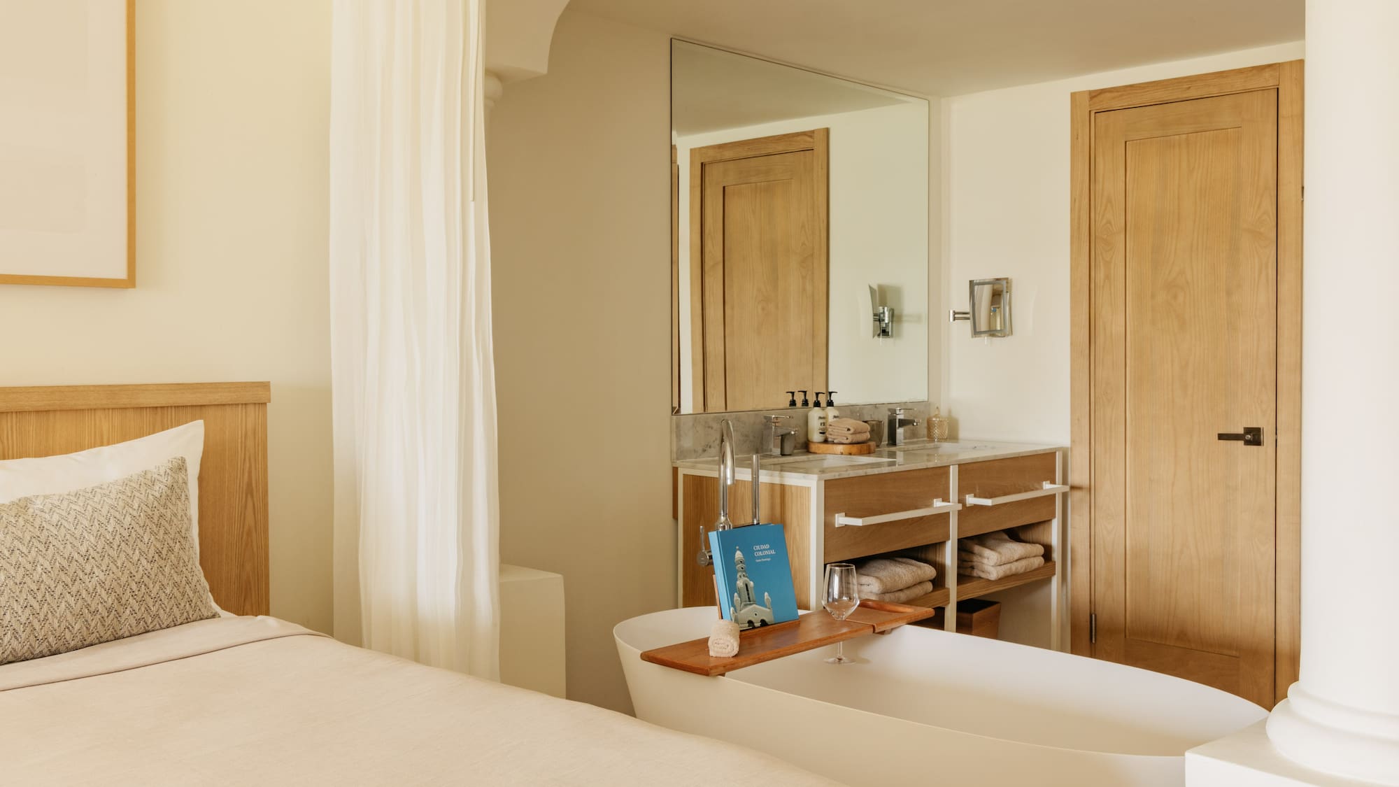 Spa-like hotel suite with bed, freestanding tub, and wooden vanity.