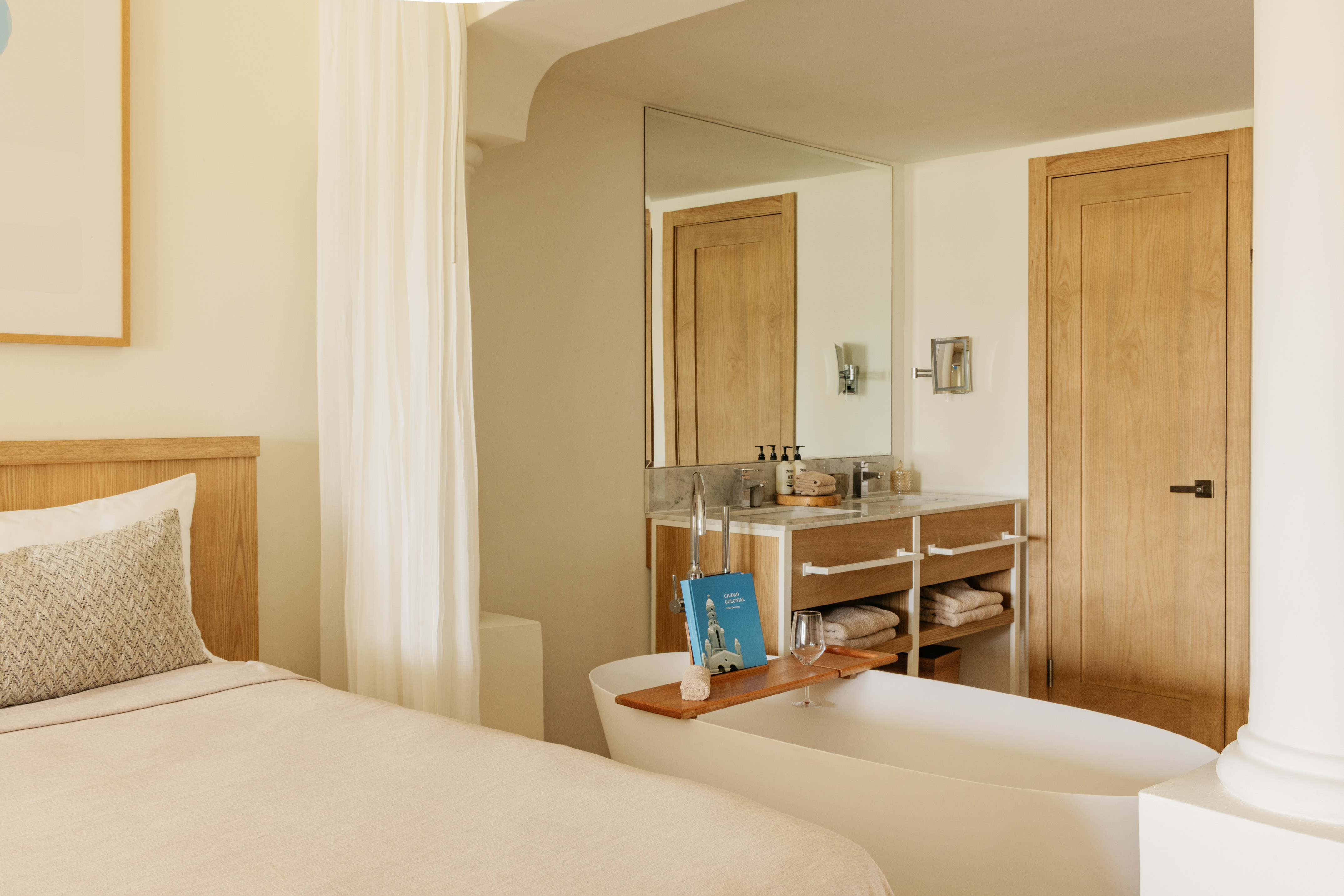 Spa-like hotel suite with bed, freestanding tub, and wooden vanity.