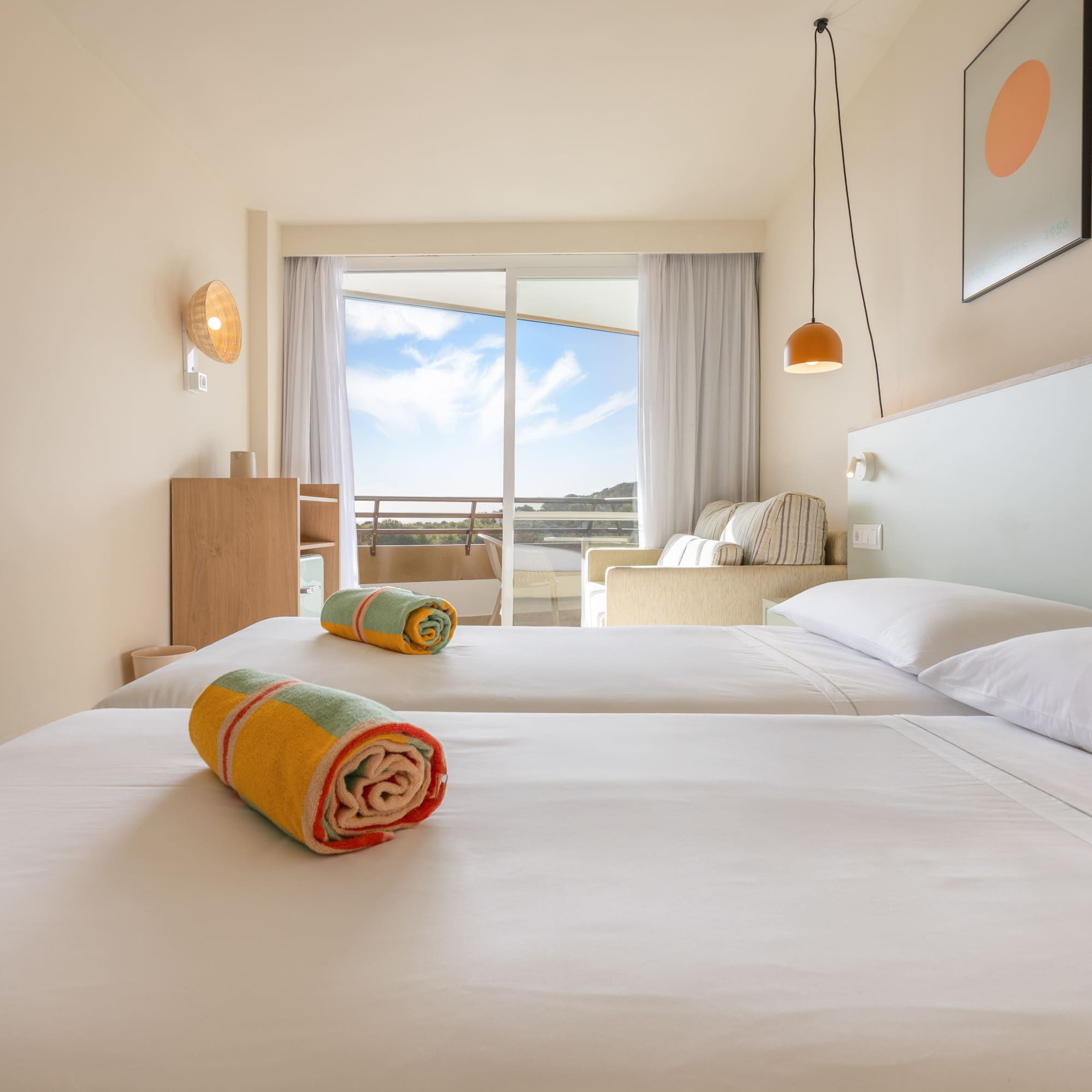 Habitación de hotel con dos camas individuales, balcón y vistas al exterior.