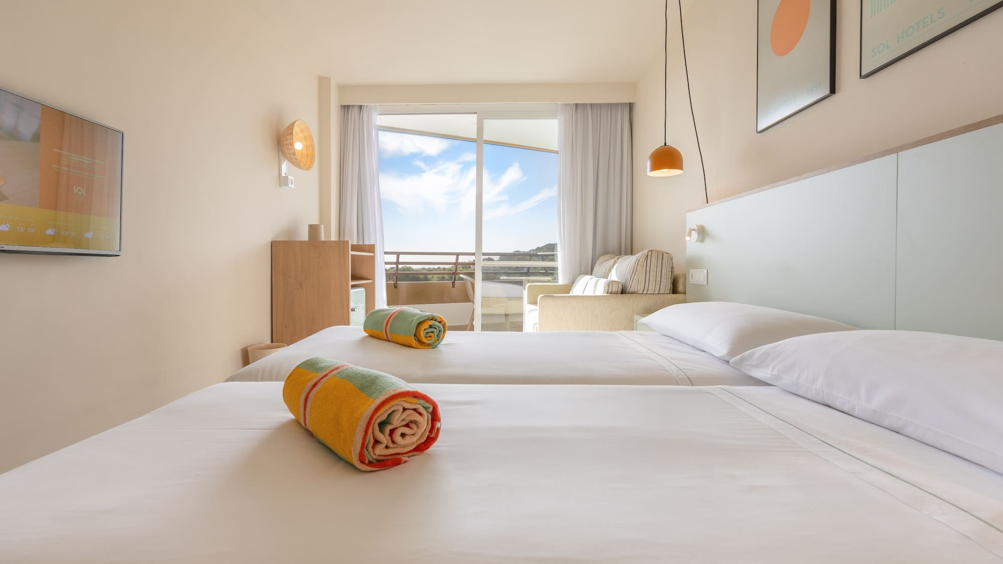 Habitación de hotel con dos camas individuales, balcón y vistas al exterior.