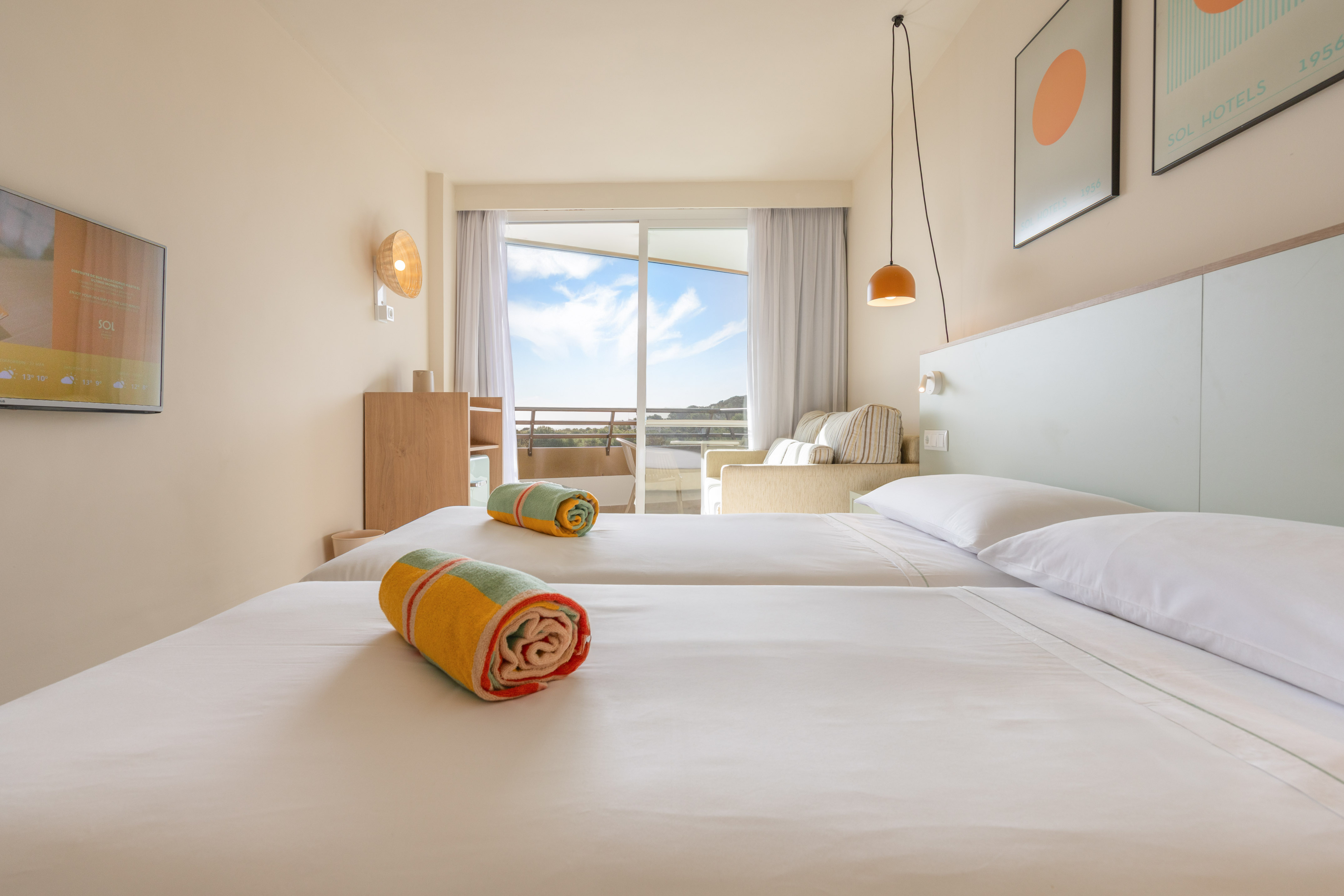 Habitación de hotel con dos camas individuales, balcón y vistas al exterior.