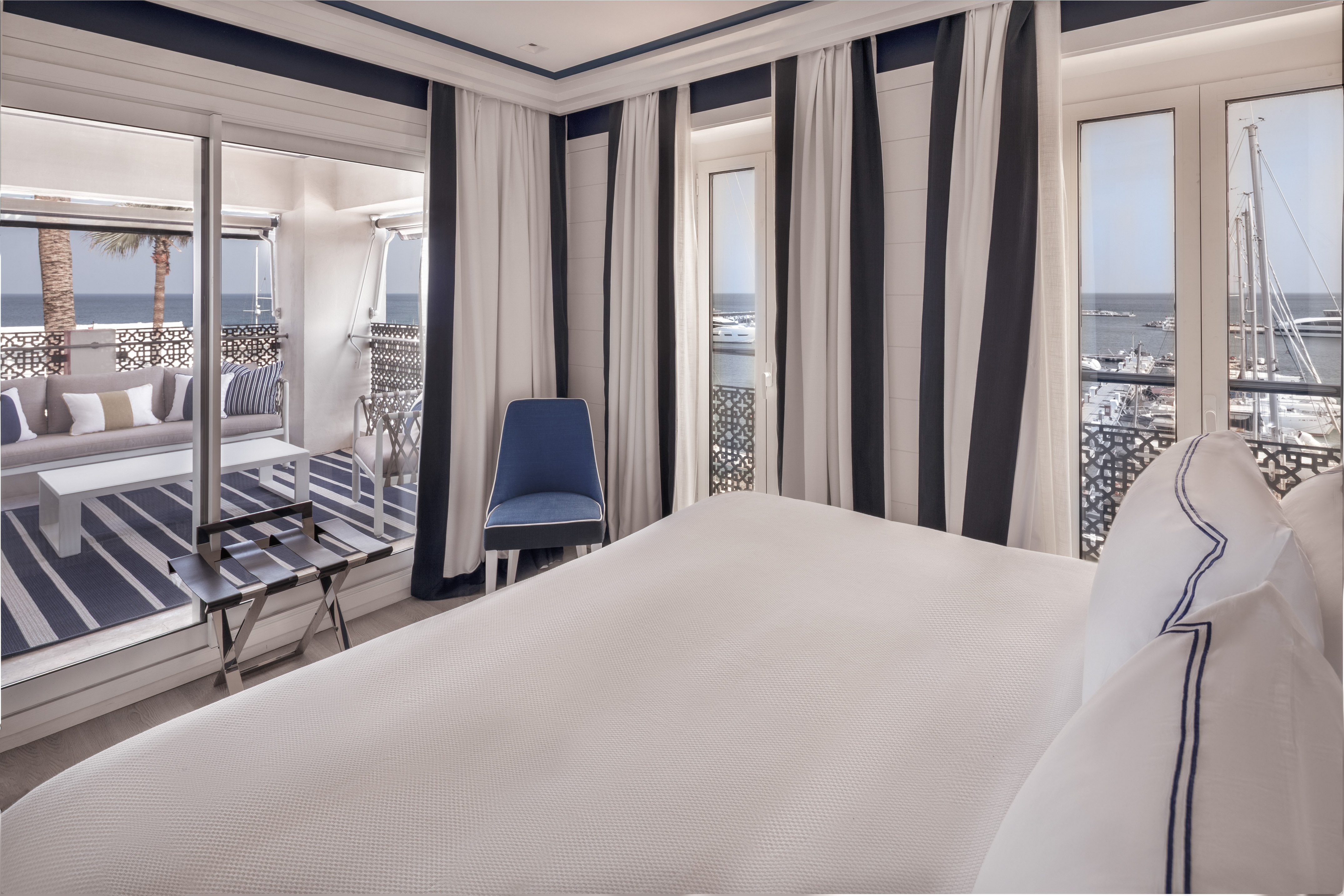 a room with a bed and chairs and a balcony overlooking the ocean