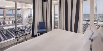 a room with a bed and chairs and a balcony overlooking the ocean