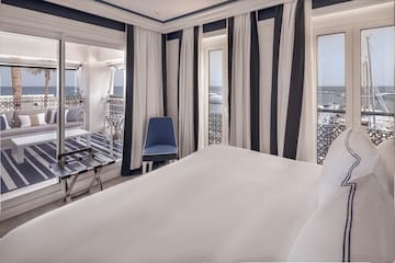 a room with a bed and chairs and a balcony overlooking the ocean