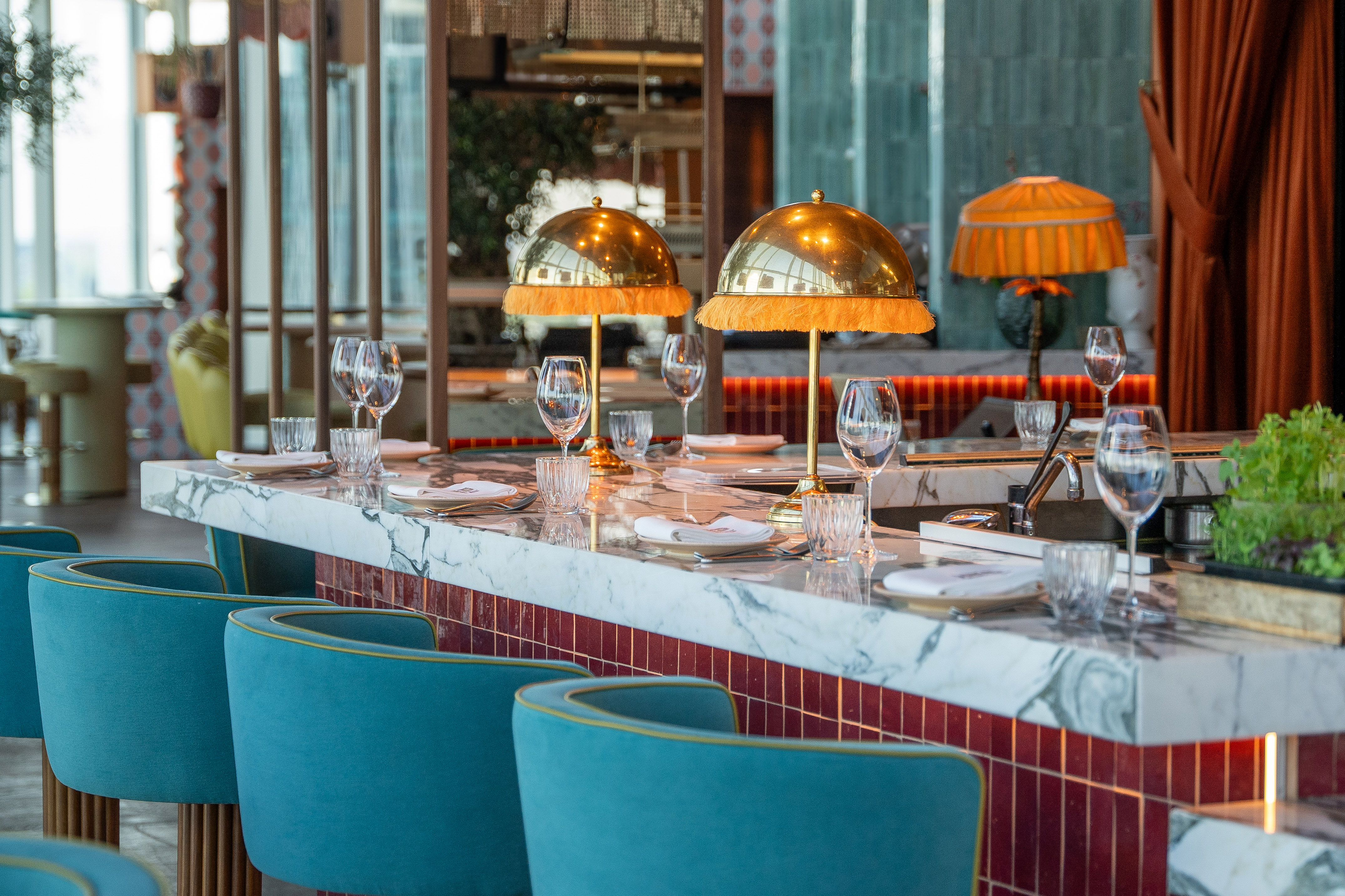 Elegant restaurant bar with marble top, teal stools, and golden dome lamps.