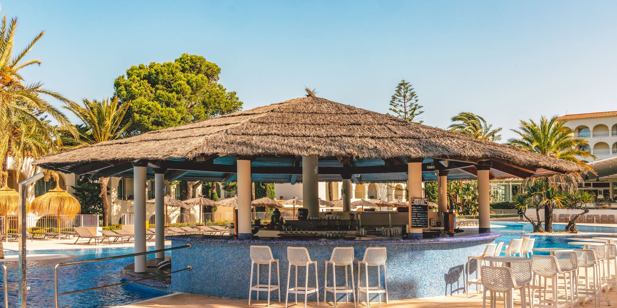 Resort swim-up bar with thatched roof and pool, surrounded by palm trees.
