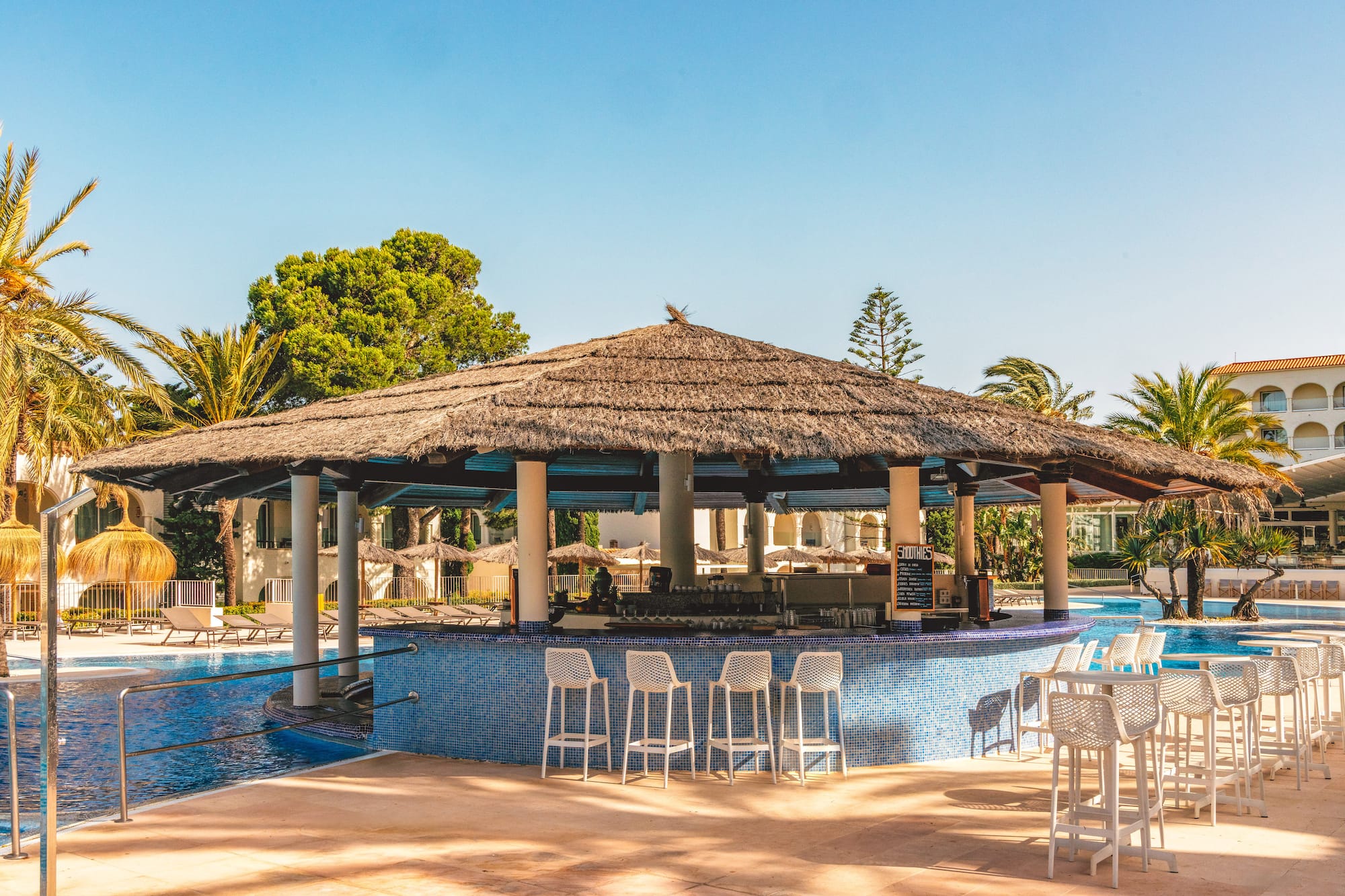 Resort swim-up bar with thatched roof and pool, surrounded by palm trees.