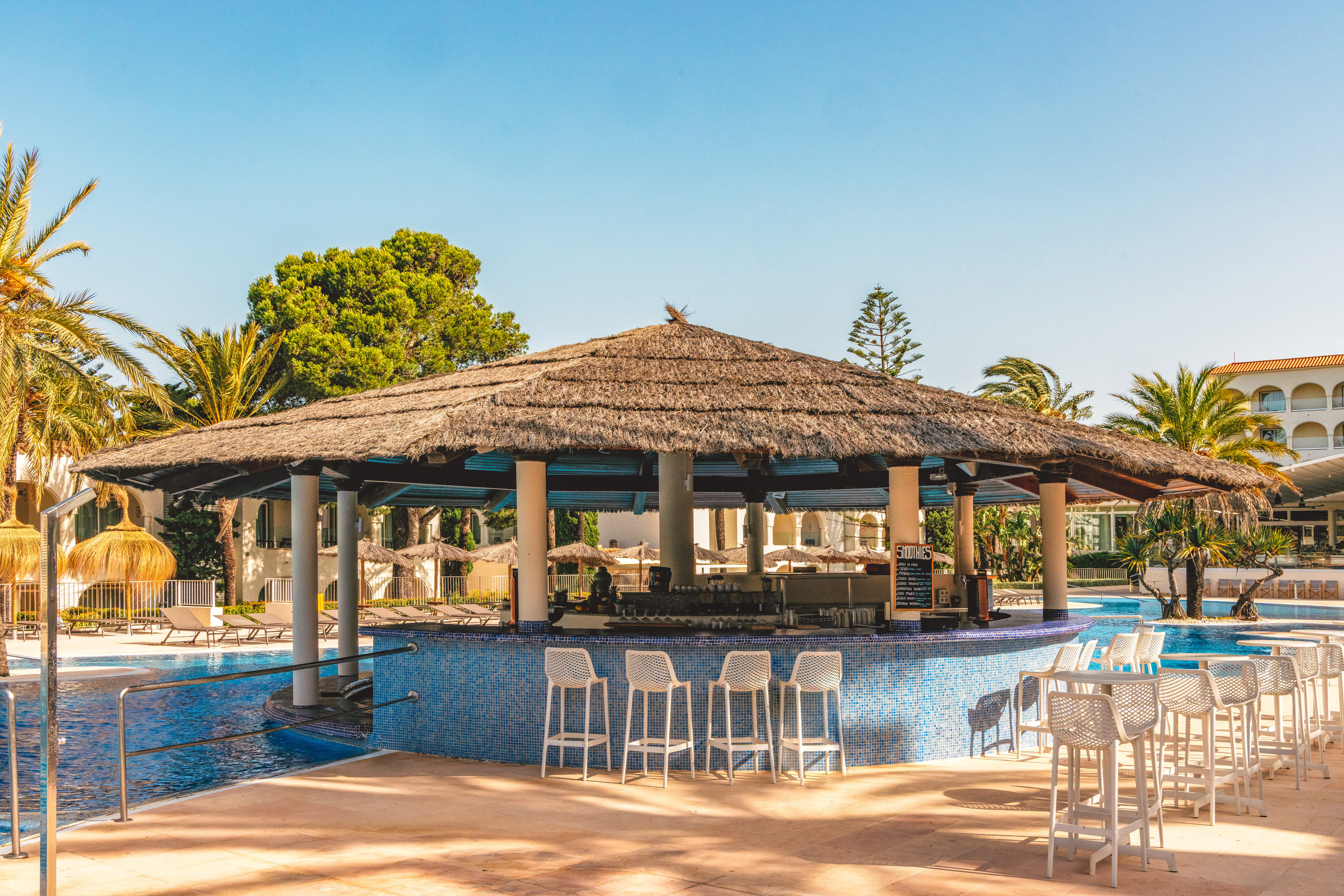 Resort swim-up bar with thatched roof and pool, surrounded by palm trees.