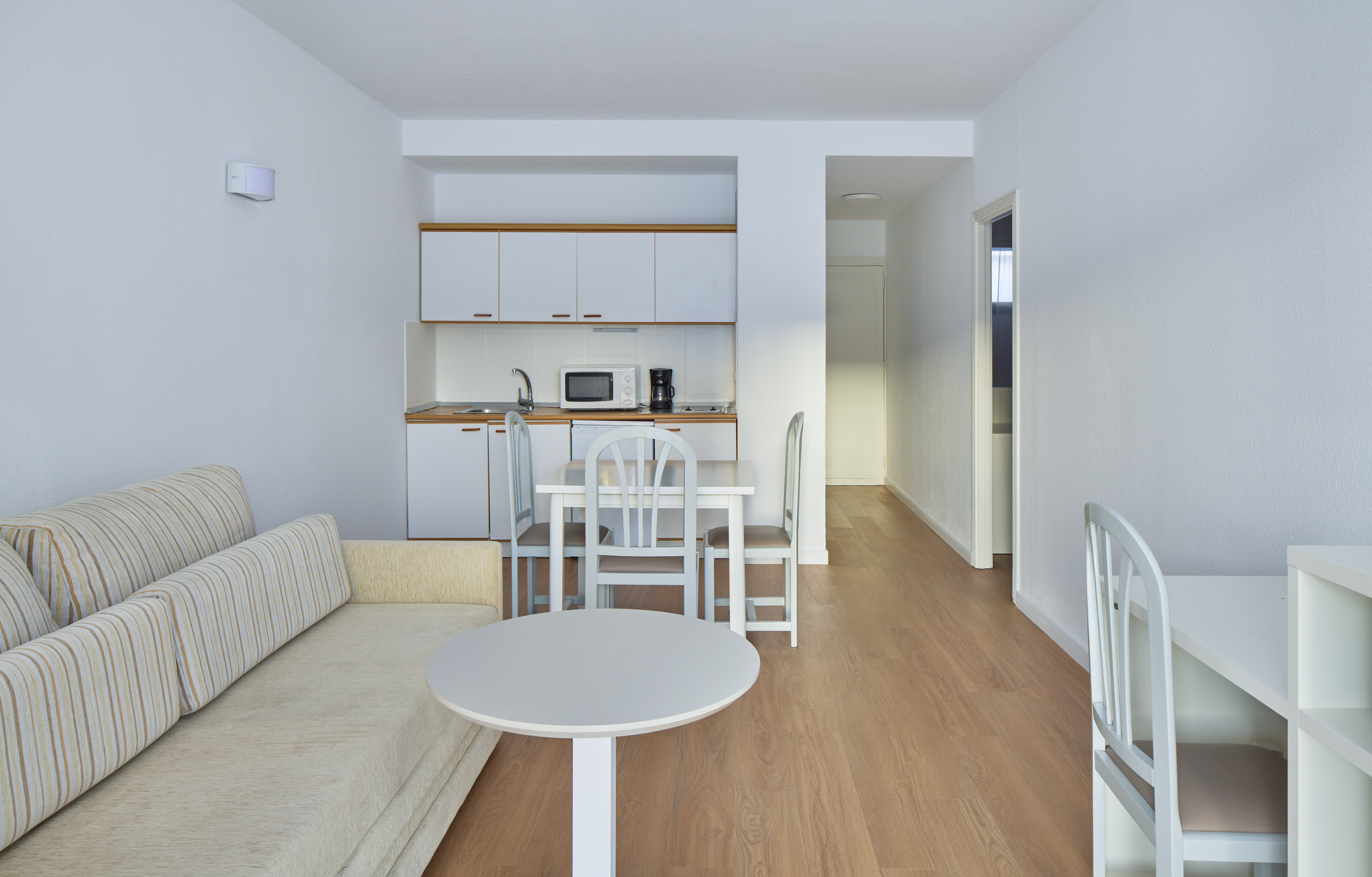 Bright hotel studio apartment with kitchenette, dining, sofa, and desk area.