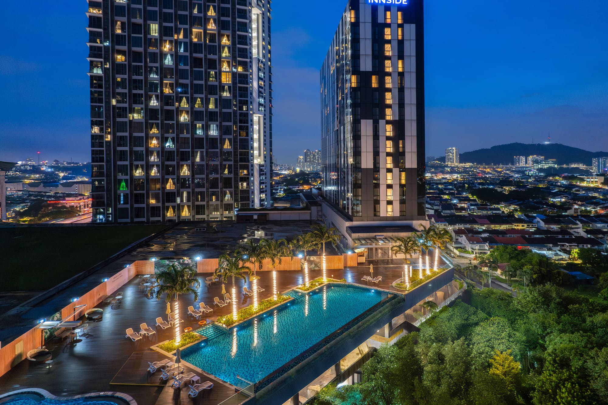INNSiDE hotel rooftop pool at night, flanked by skyscrapers with city skyline.