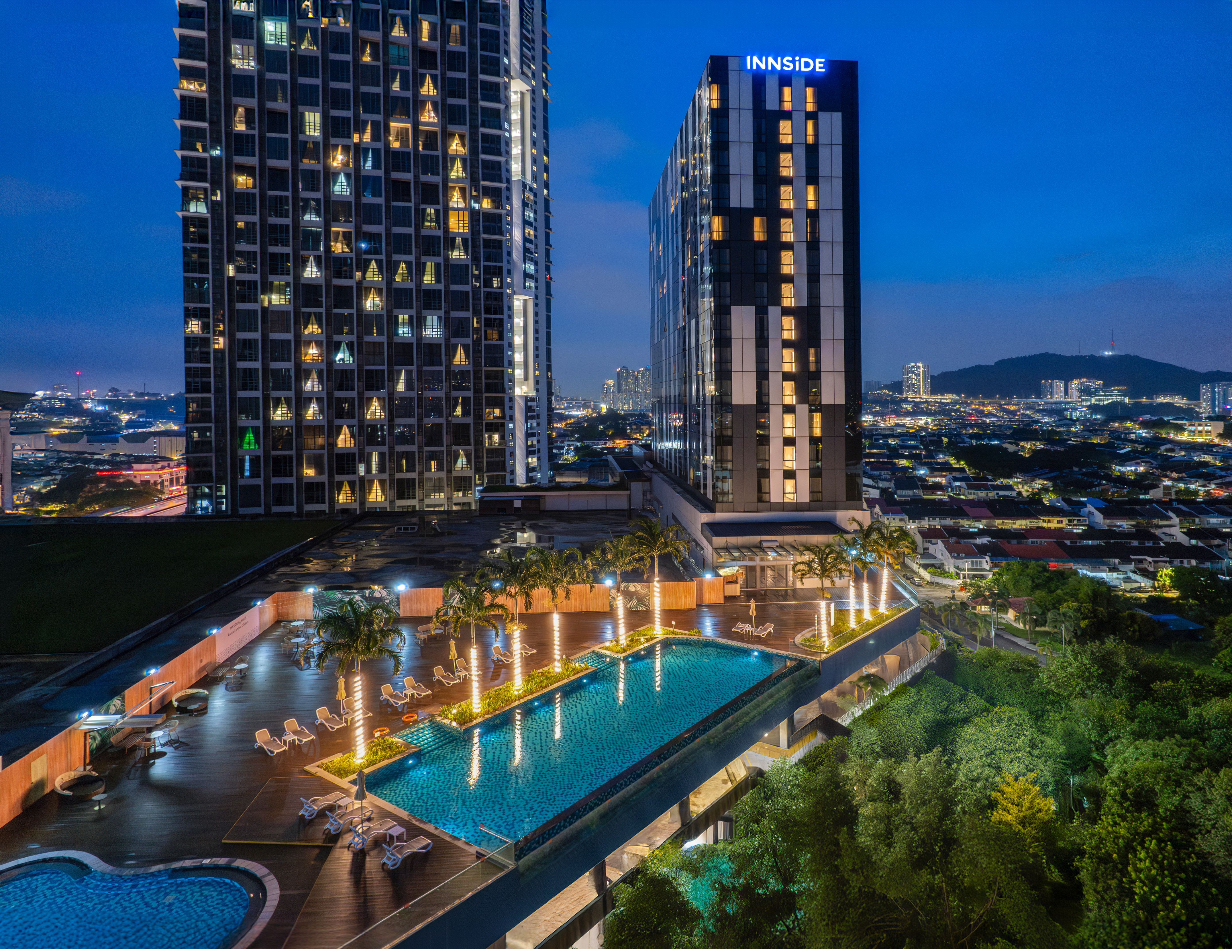 INNSiDE hotel rooftop pool at night, flanked by skyscrapers with city skyline.