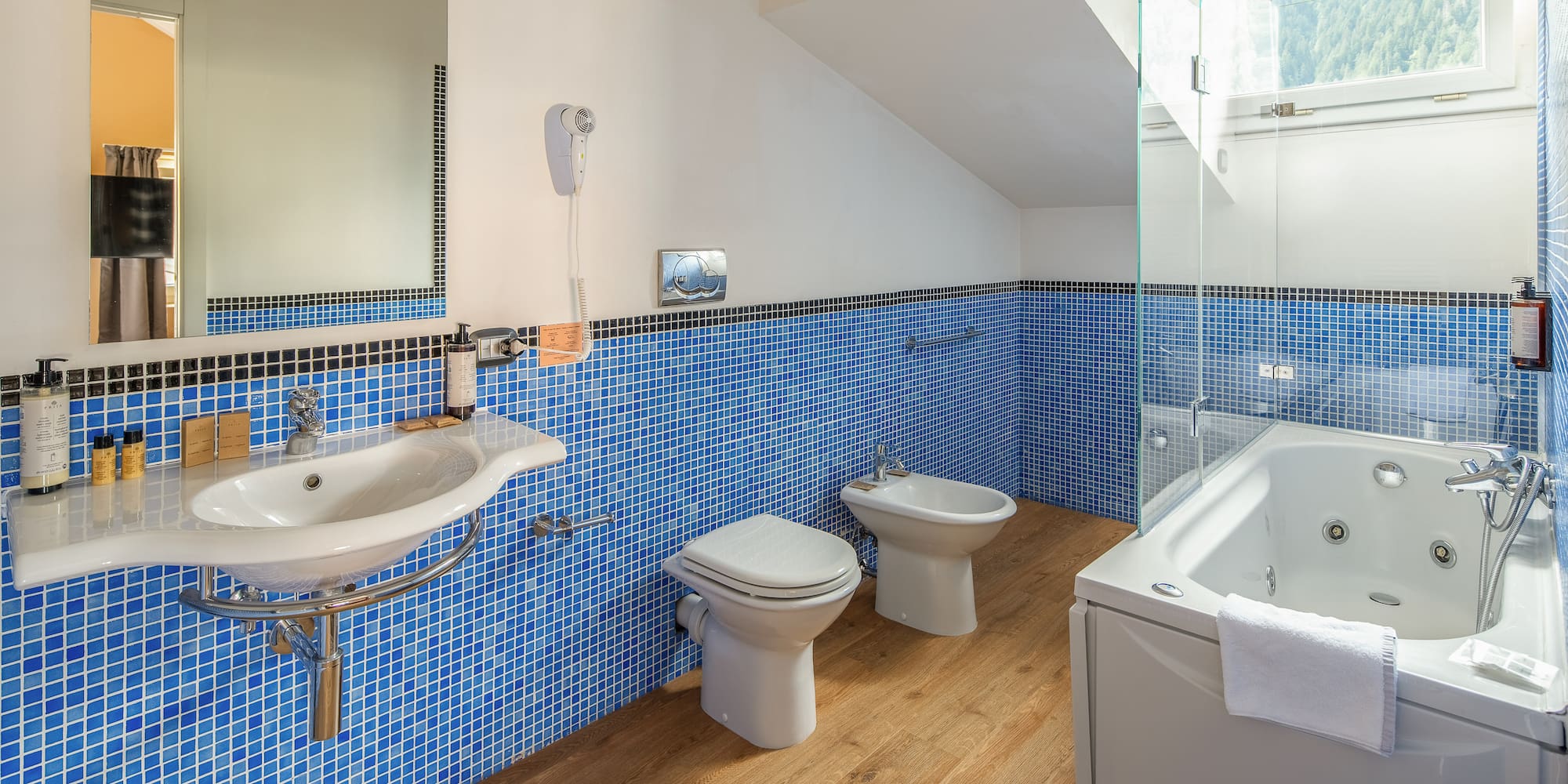 Modern blue tiled bathroom with jacuzzi tub, sink, toilet, and bidet.